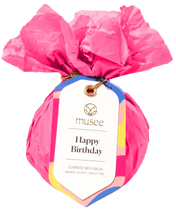 Pink bath bomb wrapped in pink tissue paper with a Musee Happy Birthday tag.