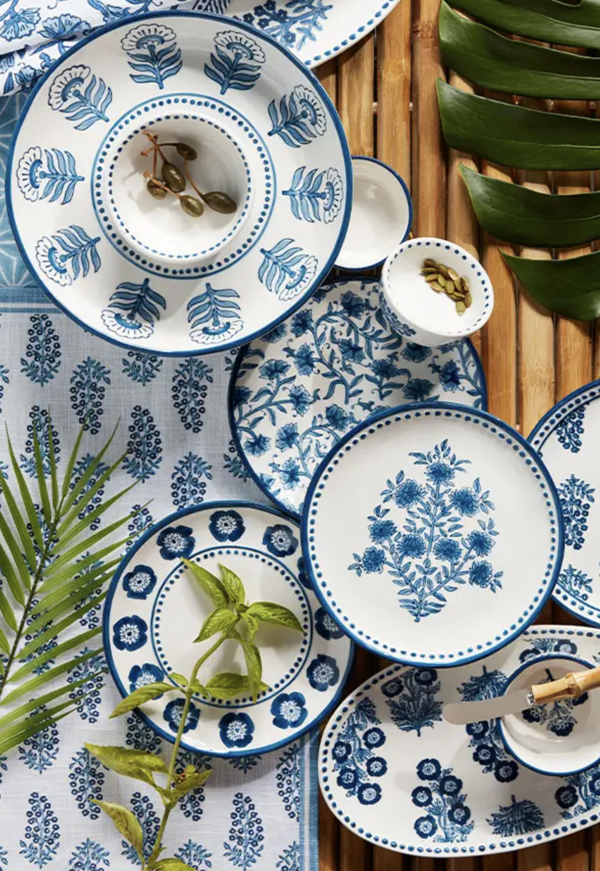 Blue and white floral patterned plates and bowls on a table with tropical leaves and greenery.