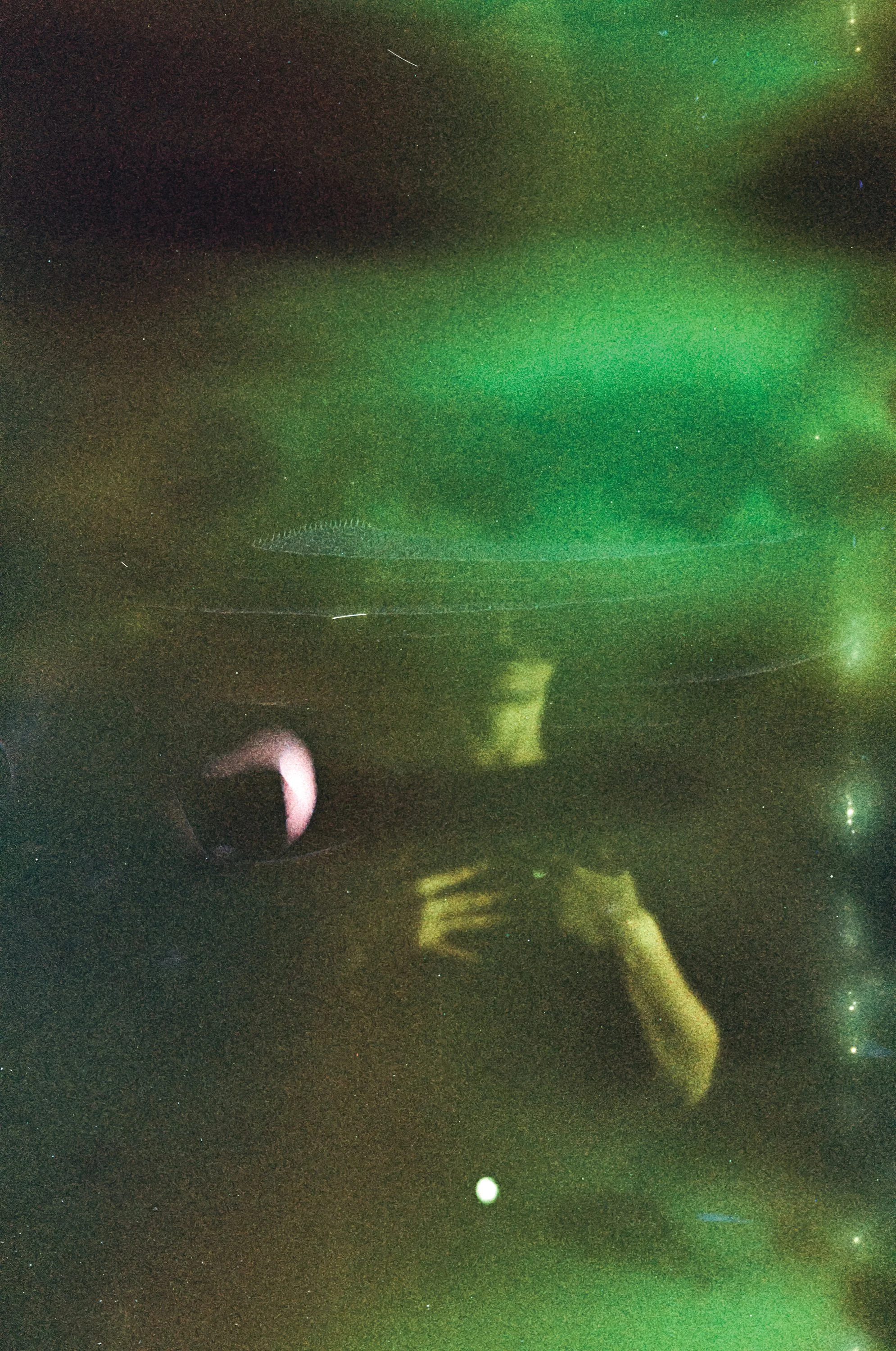 Night sky featuring an aurora with green and purple hues, stars, and a silhouette of a person taking a photo with a camera.