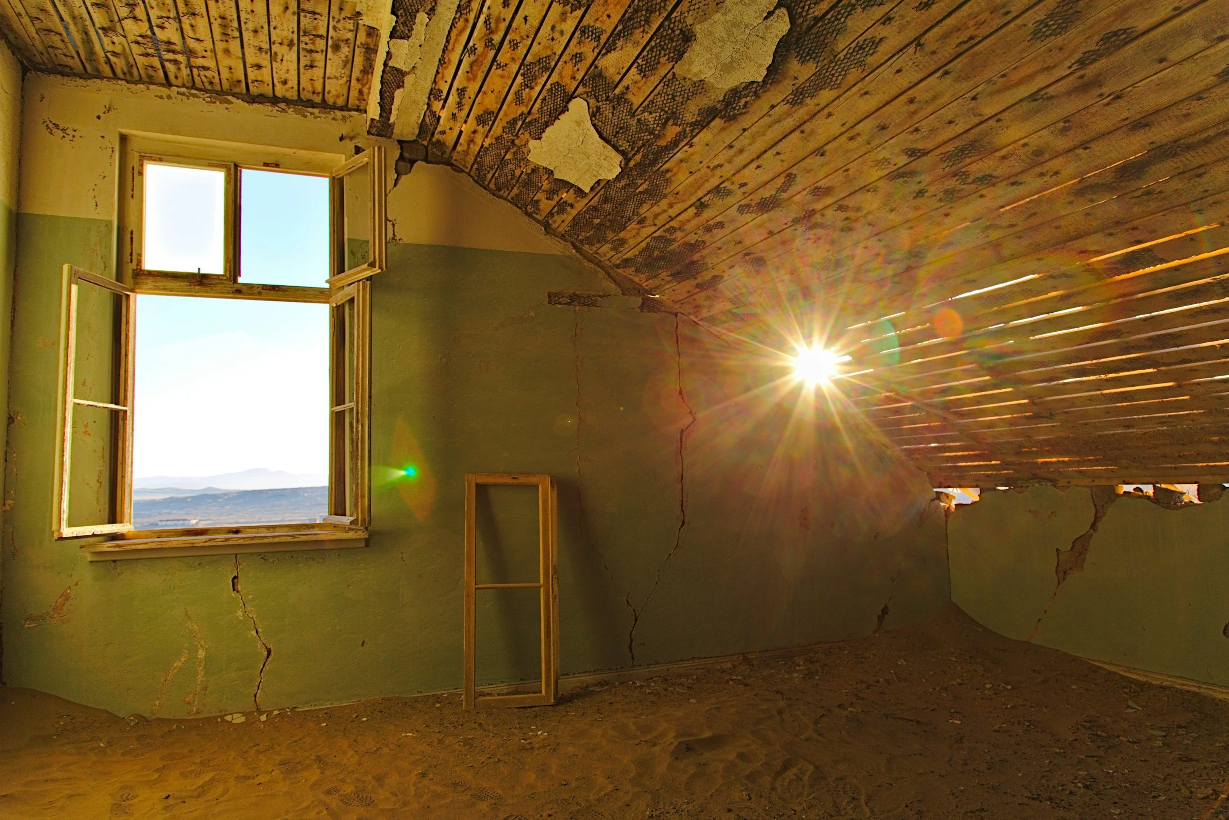 An abandoned room with cracked green walls, a rooftop window open to sunlight, and a slanted wooden ceiling with peeling paint, sunlight shining through creating a lens flare.
