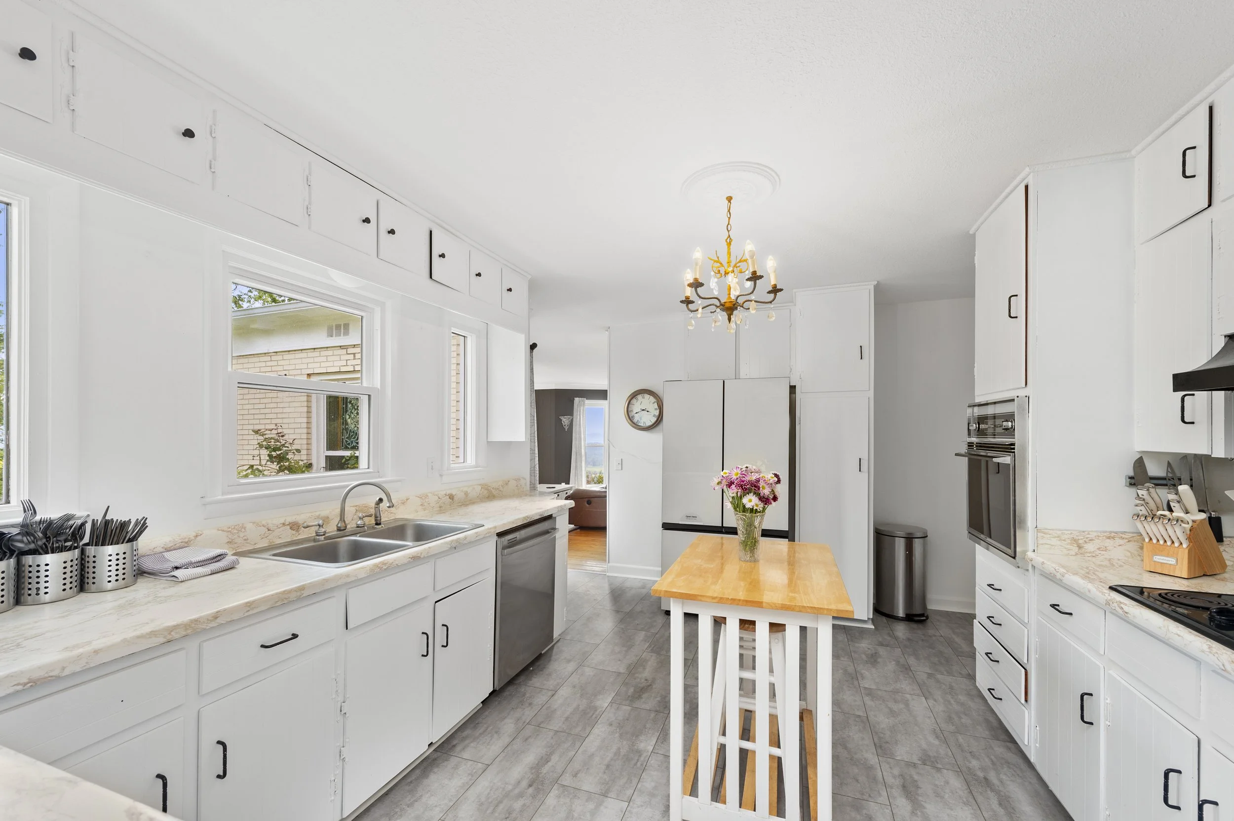 Modern kitchen with white cabinets, wooden island, stainless steel appliances, and chandelier. Wedding kitchen catering
