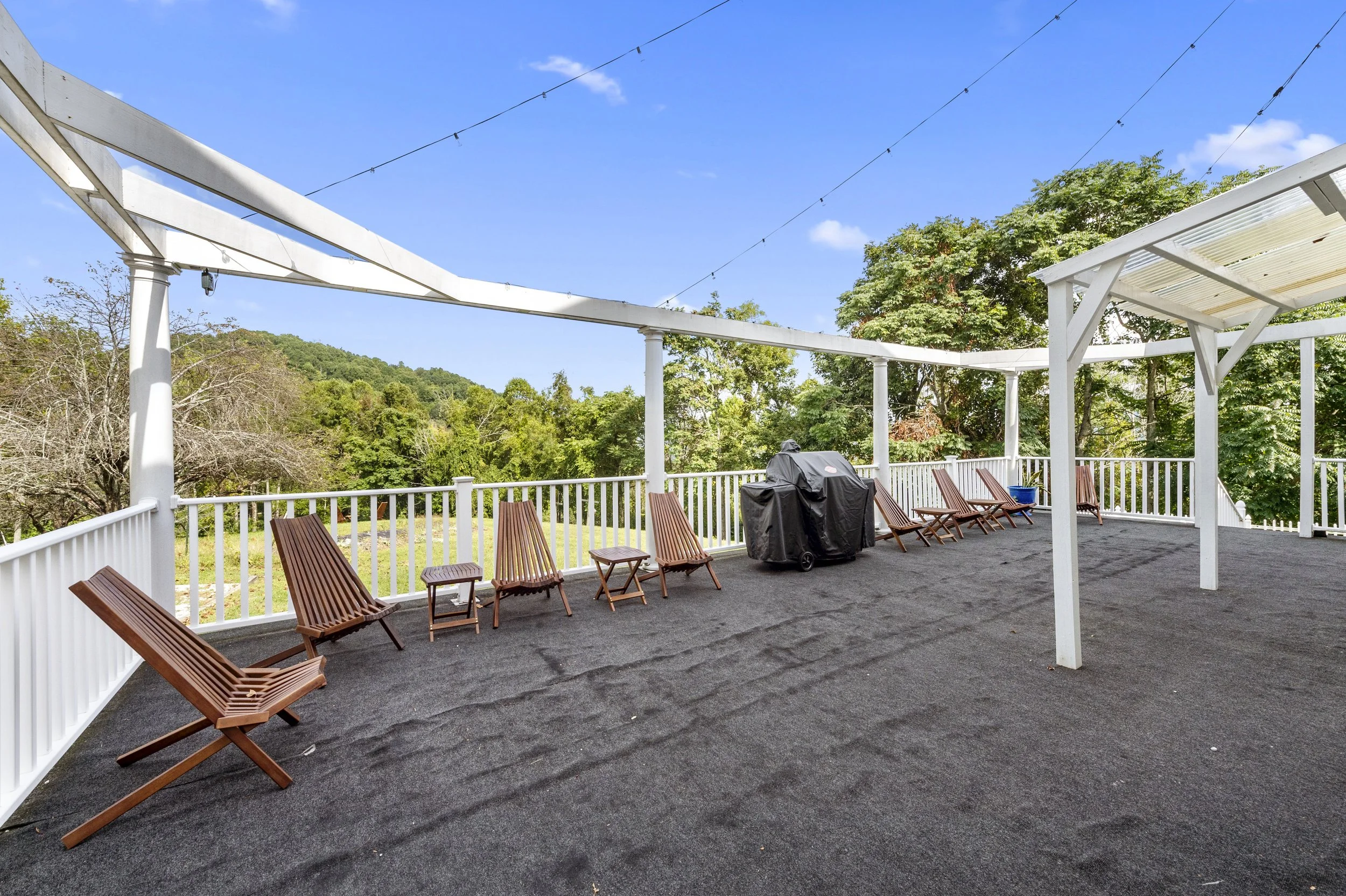 Outdoor deck with lounge chairs, grill, and string lights under clear sky. perfect wedding location for reception.