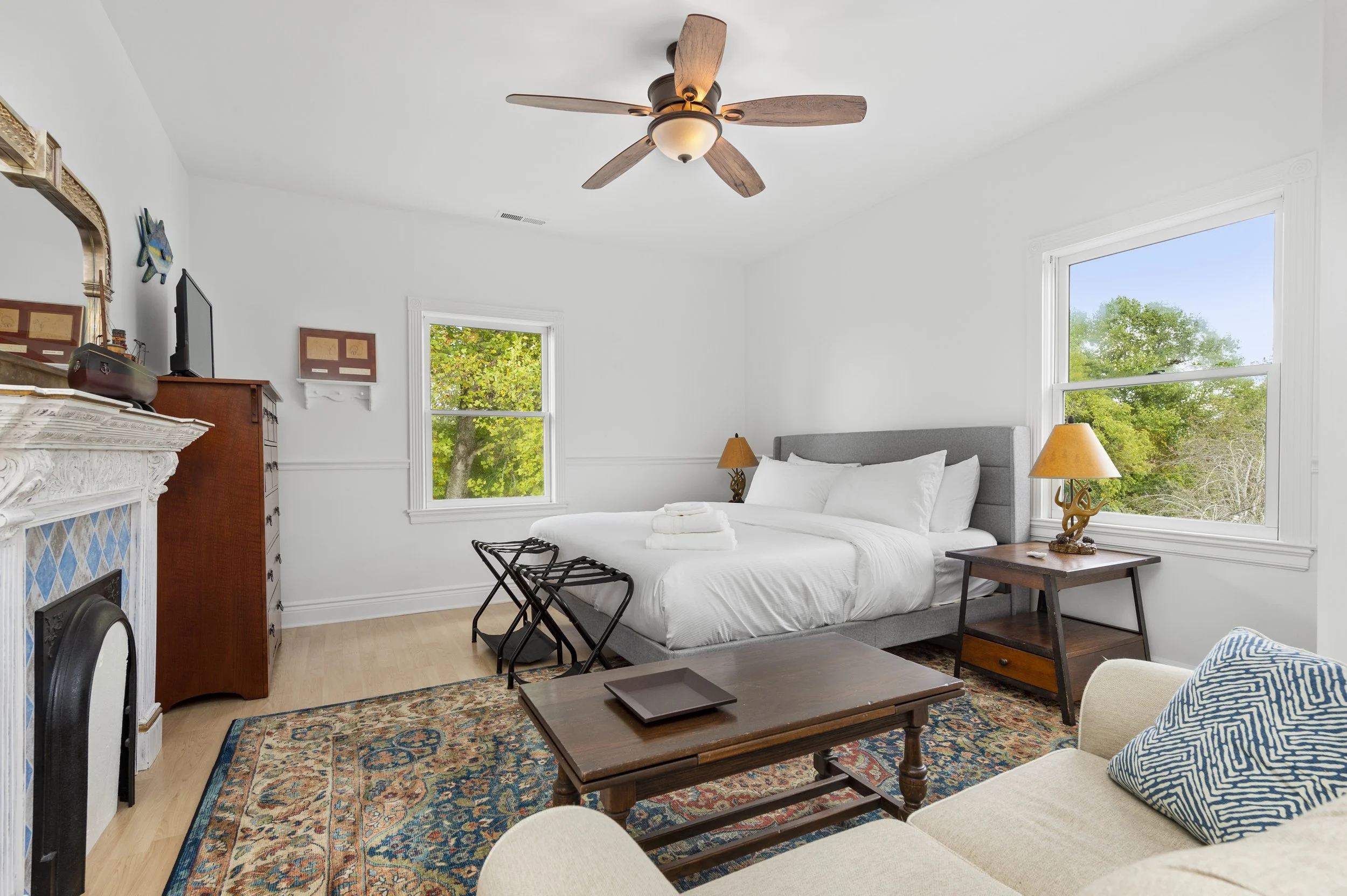 Bright bedroom with a white bed, ceiling fan, wooden furniture, and a colorful area rug.