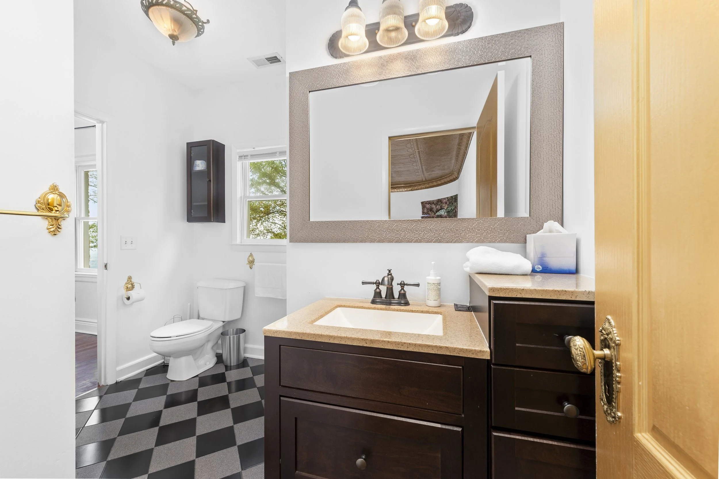 Modern bathroom with dark wood vanity, large mirror, toilet, and black and white checkered floor.