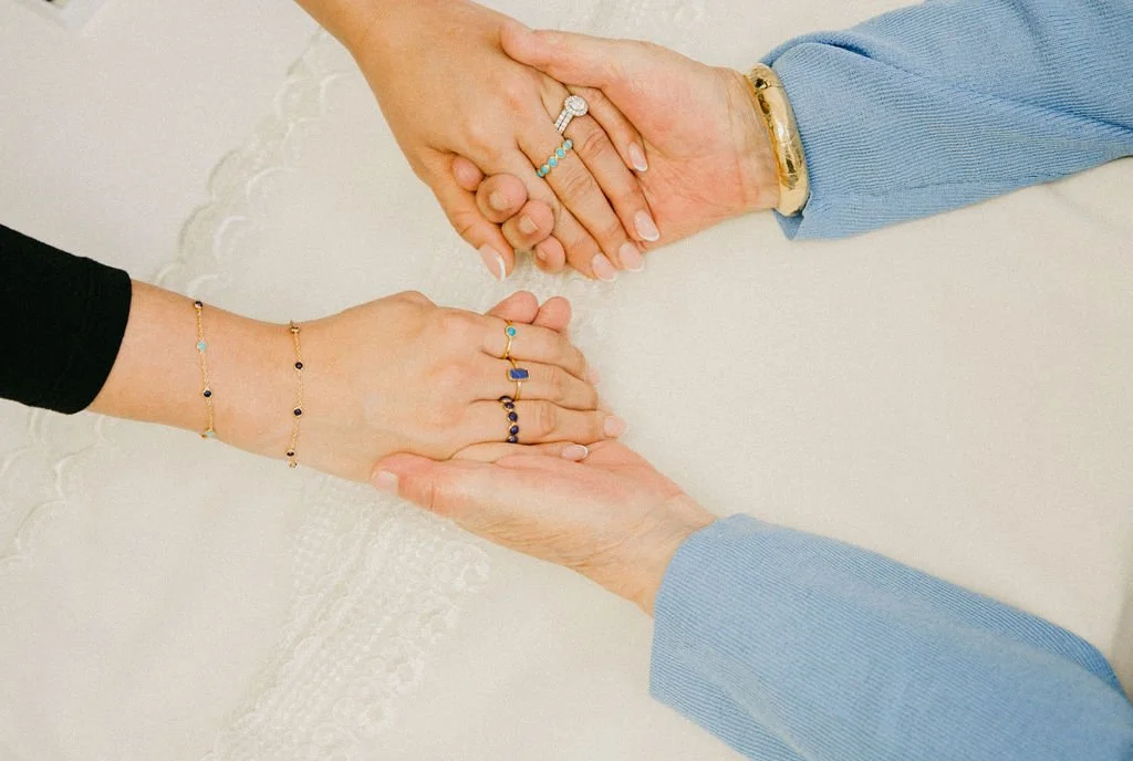 Close-up of two people holding hands while wearing gold jewelry with turquoise and lapis stones.