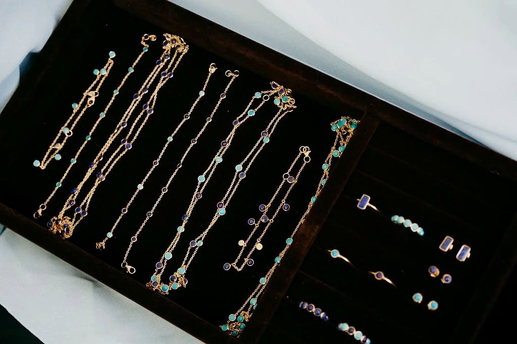 Jewelry tray displaying gold necklaces, bracelets, rings, and earrings featuring turquoise and lapis-toned stones.