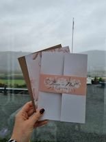 Hand holding three elegant wedding invitations with a scenic outdoor backdrop.