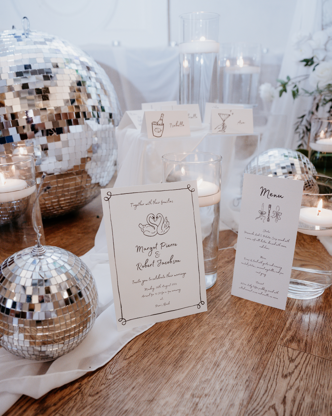 Wedding invitation and menu card on a wooden floor with disco balls and candles.