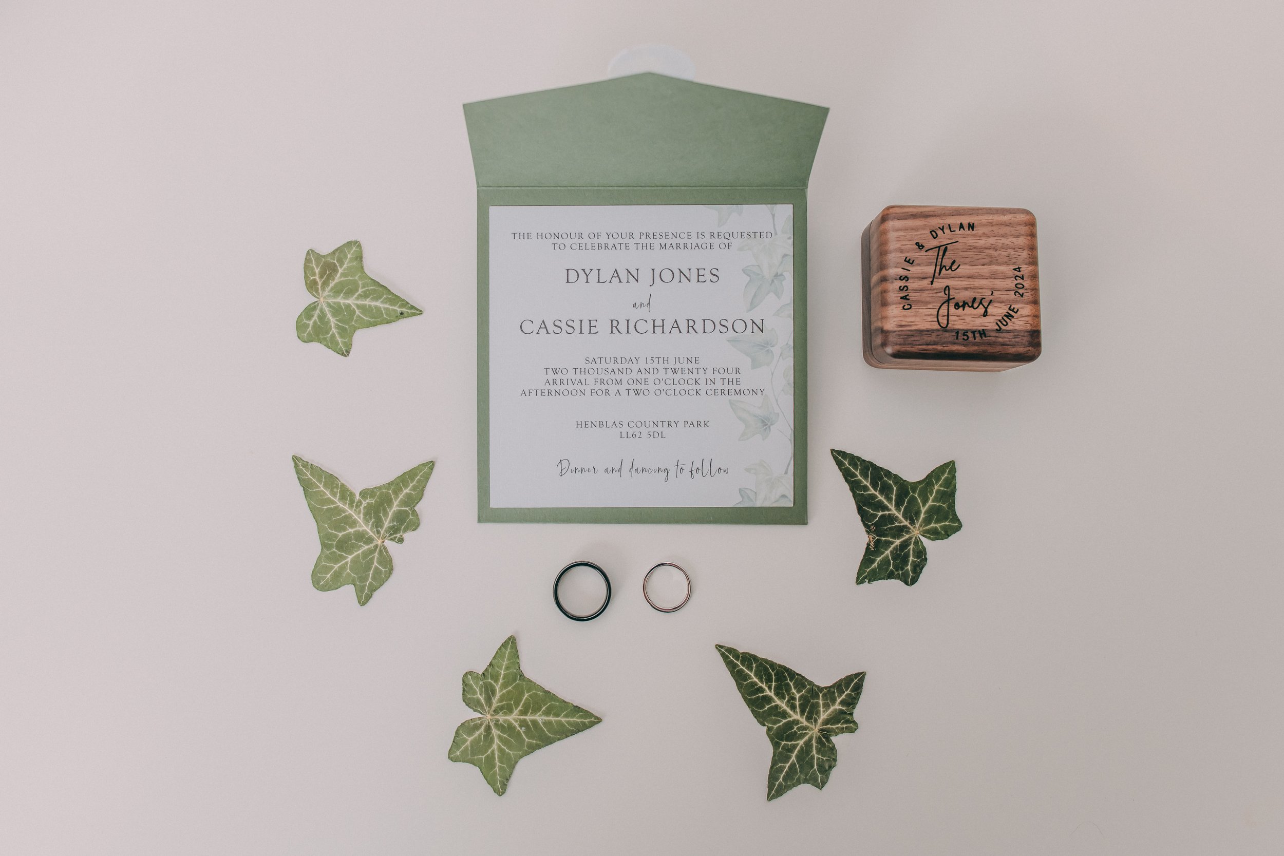 Wedding invitation with eucalyptus leaves, two rings, and a wooden box on a white background.