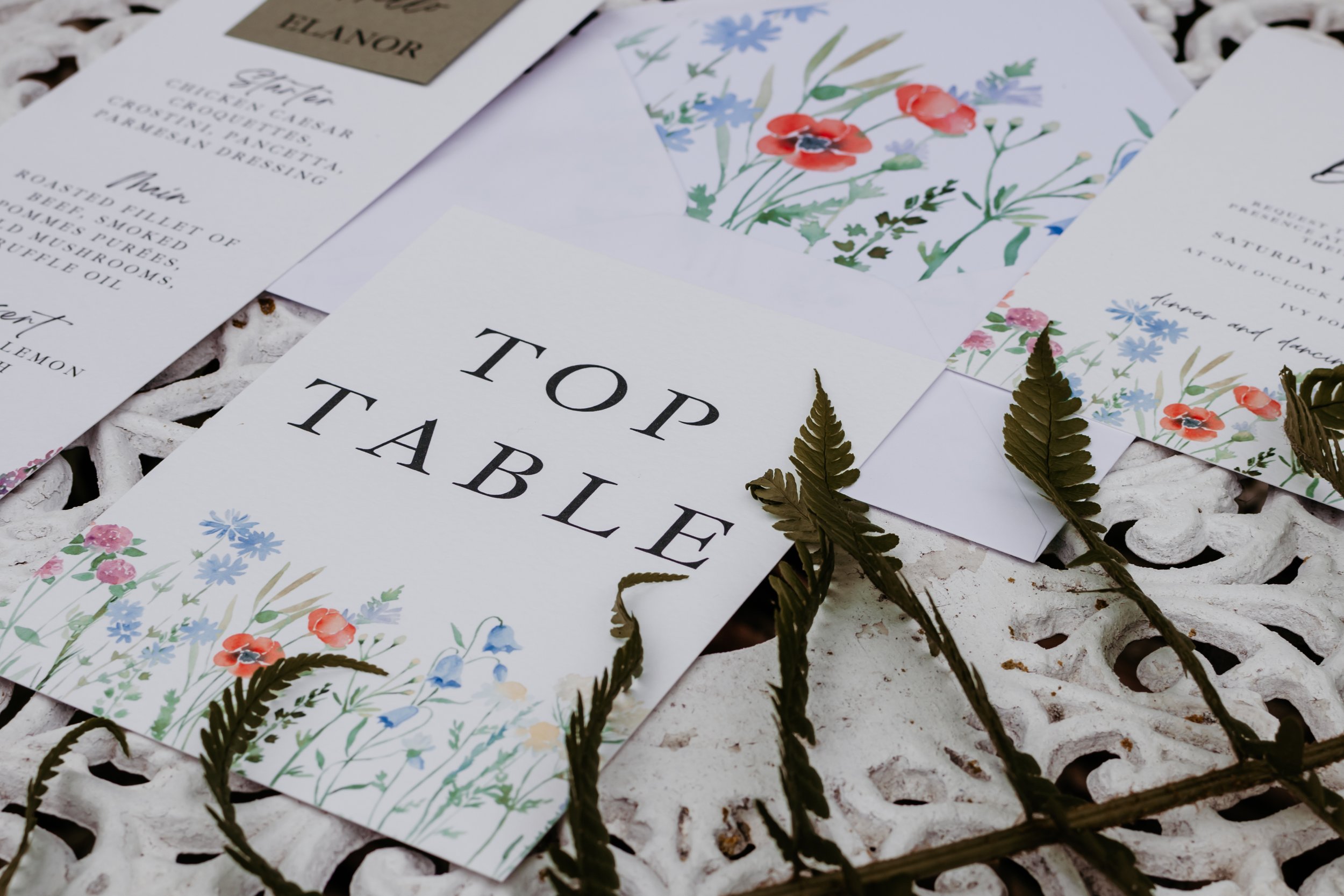 Wedding table stationery with "Top Table" printed card, floral designs, and menu on decorative surface.