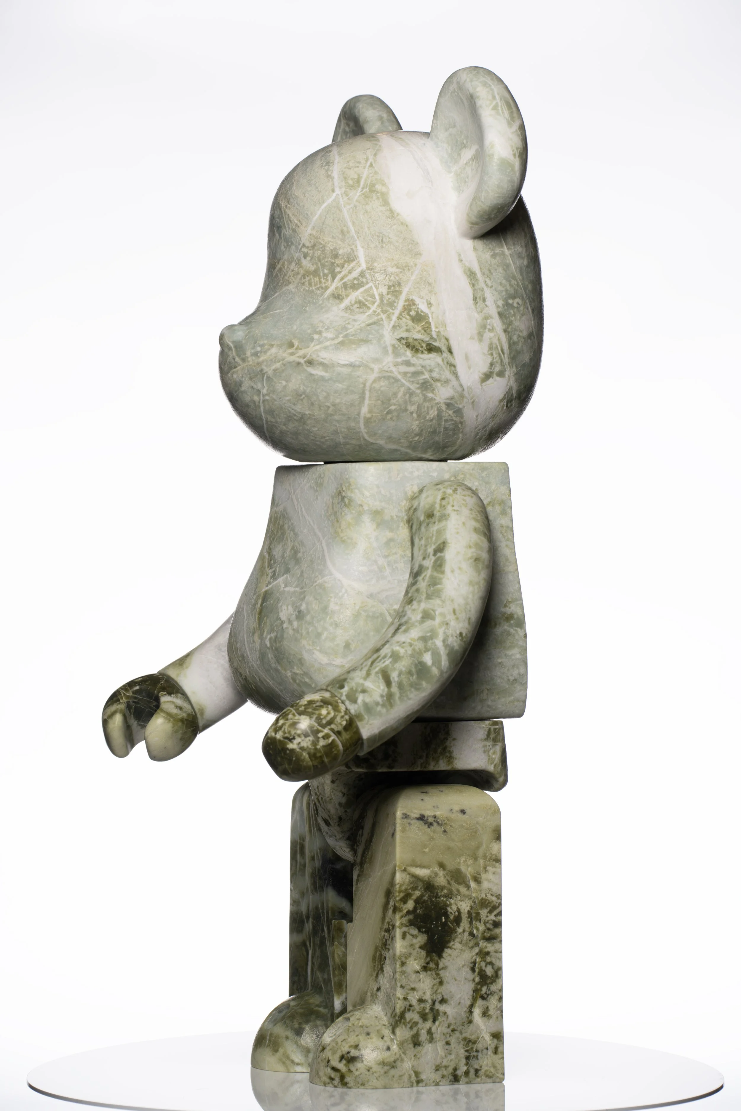 Skulptur eines sitzenden Affen aus grünem Marmor, auf einem runden weißen Sockel, frontal fotografiert.