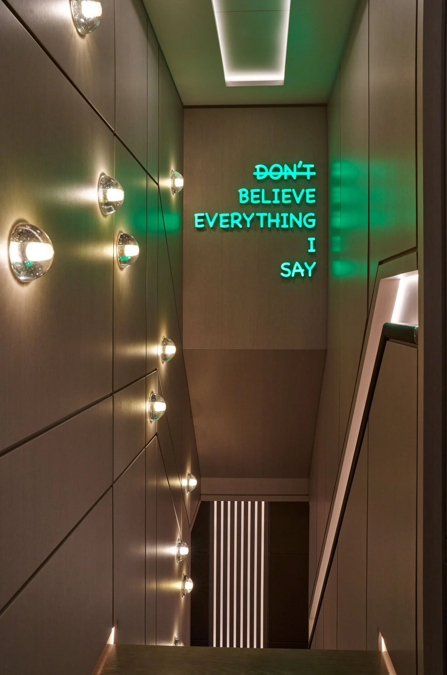 Bild eines Flurs mit Blenden und einer leuchtenden Neon-Schrift, die sagt: "DON'T BELIEVE EVERYTHING I SAY".