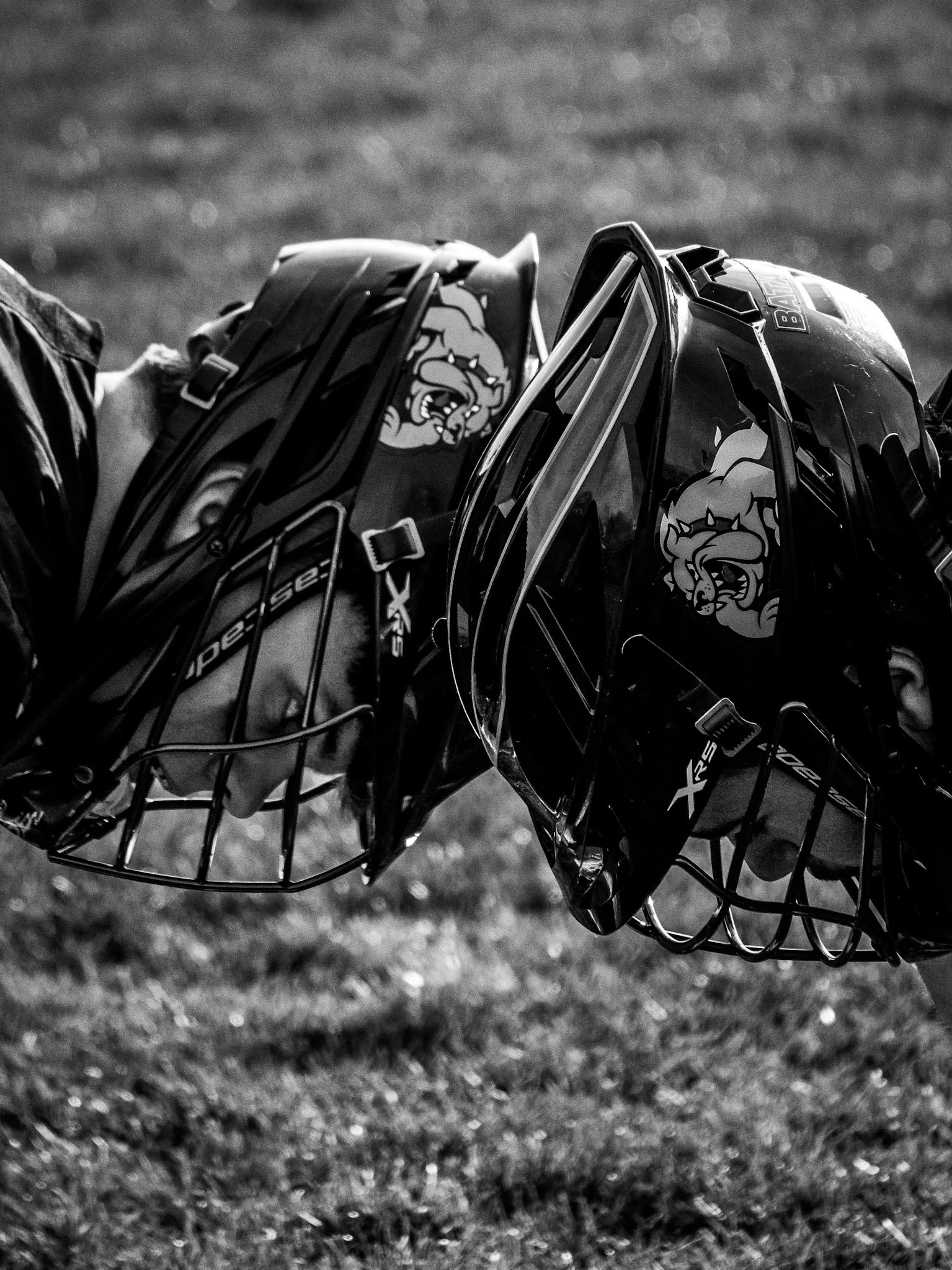 Two hockey goaltender helmets with hockey masks and team logos, facing each other outdoors on grass.