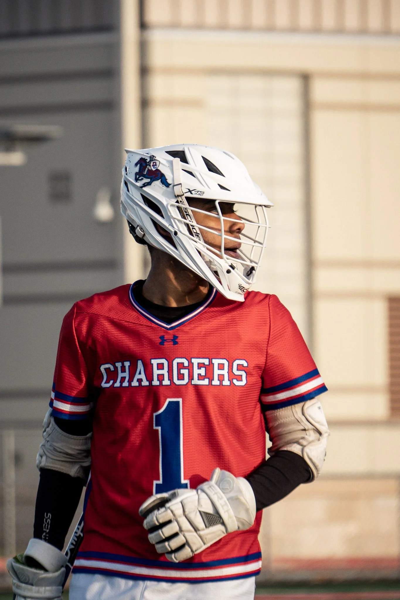 A football player wearing a red jersey with the word 'Chargers' and the number 1, a white helmet with a blue charging bull logo, and white gloves, standing outdoors.