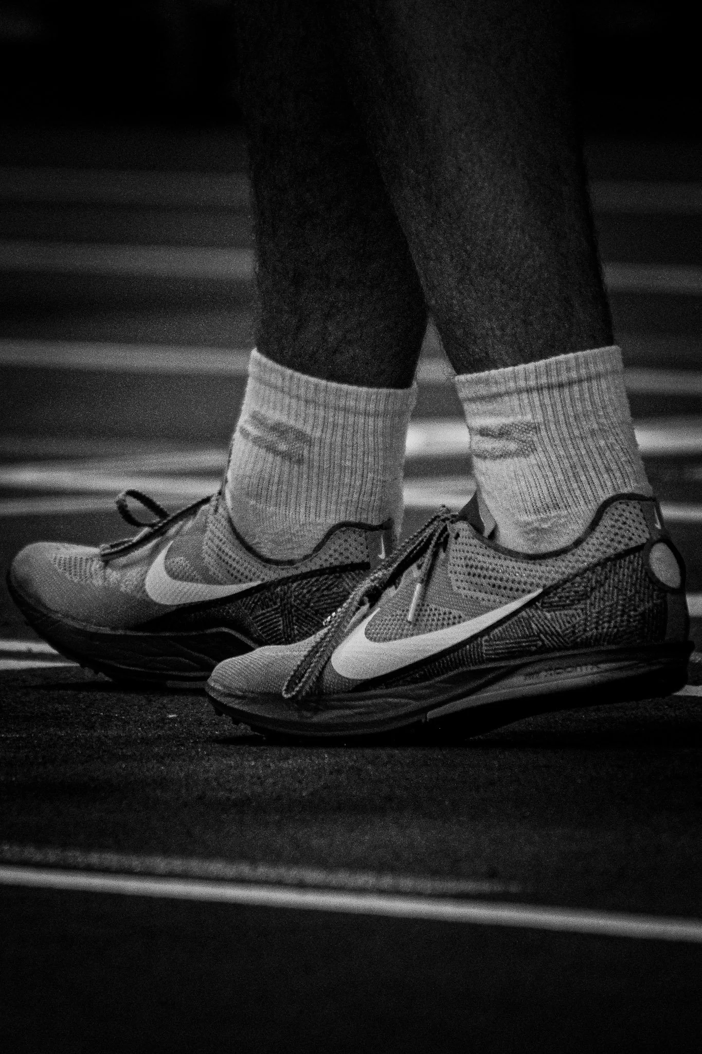 Close-up of a person's feet wearing Nike running shoes, gray socks, and dark pants, on a running track.