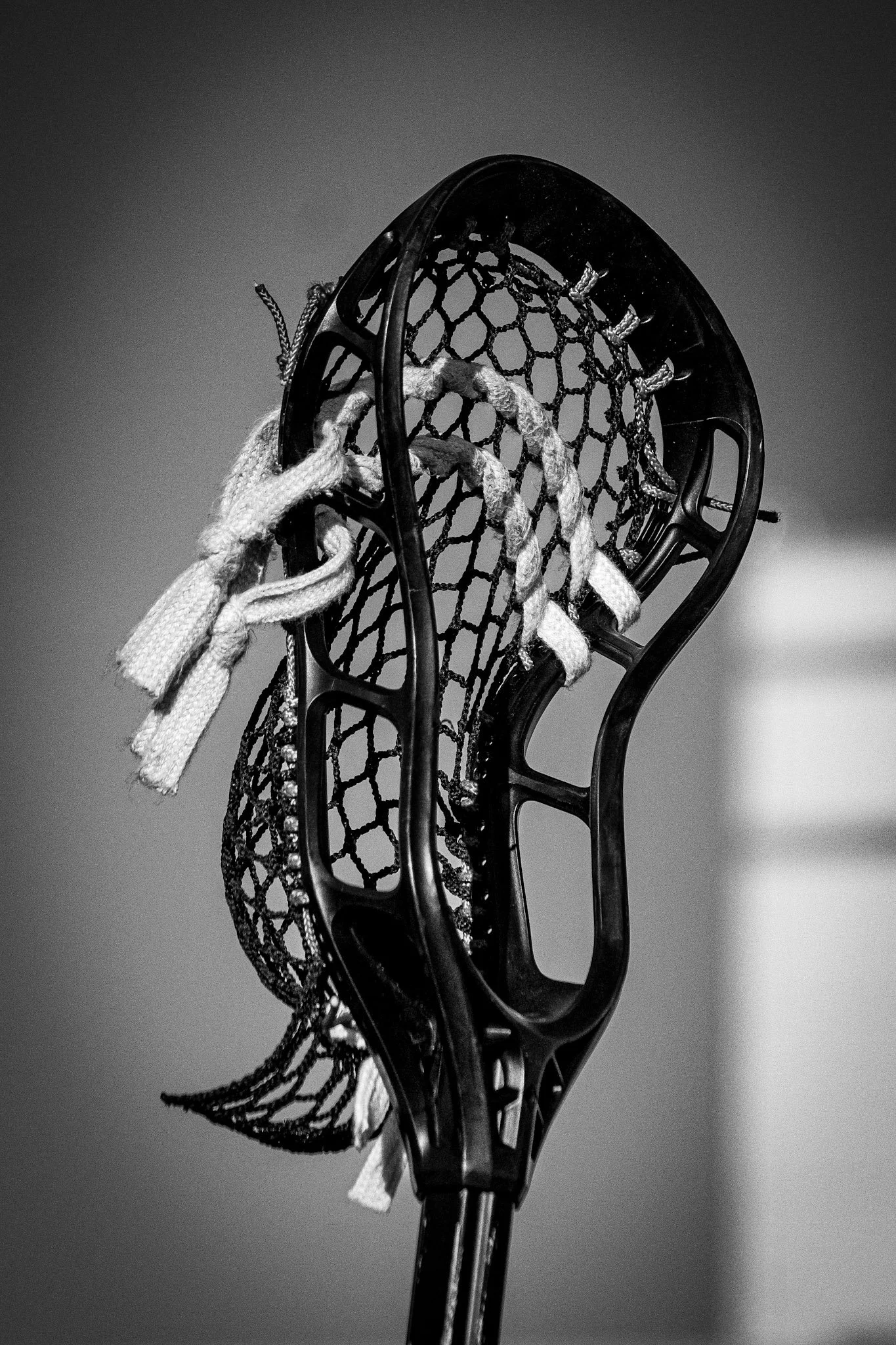 Close-up view of a lacrosse stick with a mesh pocket and attached strings, isolated on a plain background.