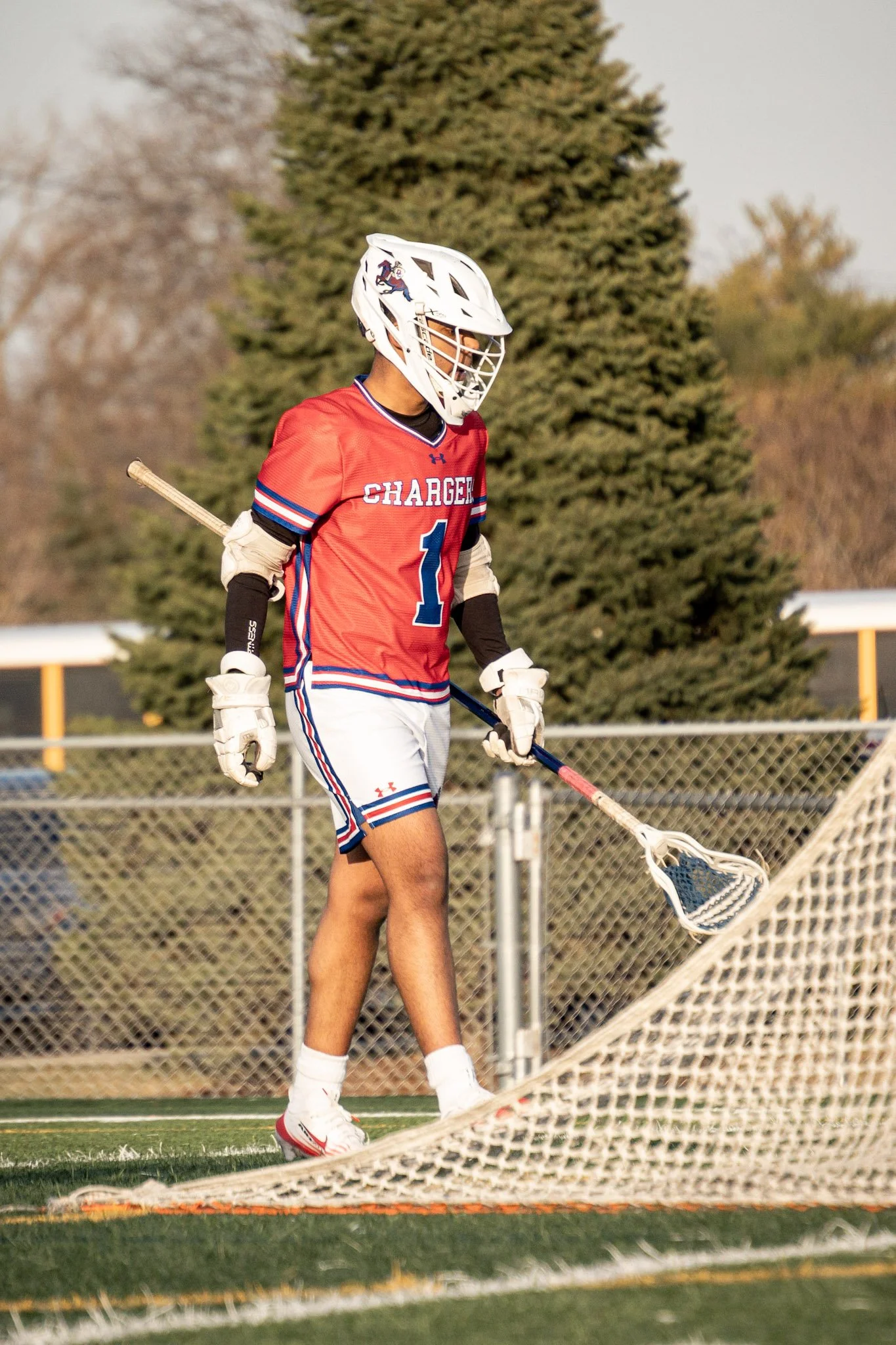 Lacrosse player in red jersey, white helmet, and white shorts on a field.