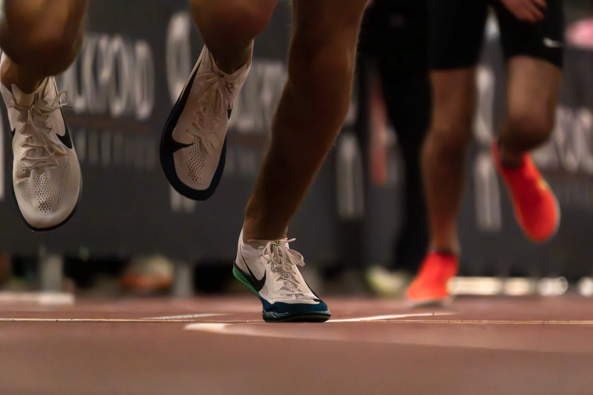 Close-up of athletes' legs during a running race, focusing on their shoes and the track.