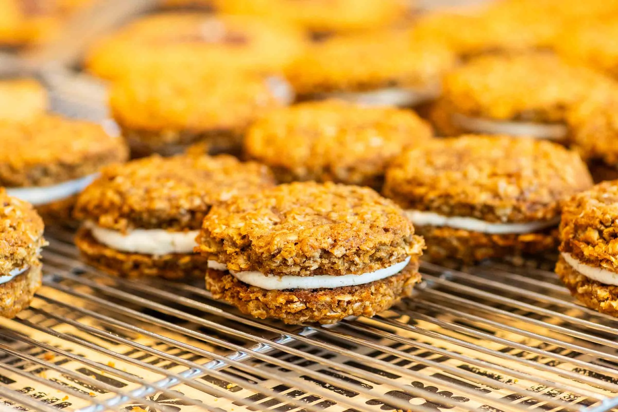 Close-up of multiple homemade oatmeal cookies with white icing in the middle, cooling on a metal wire rack.