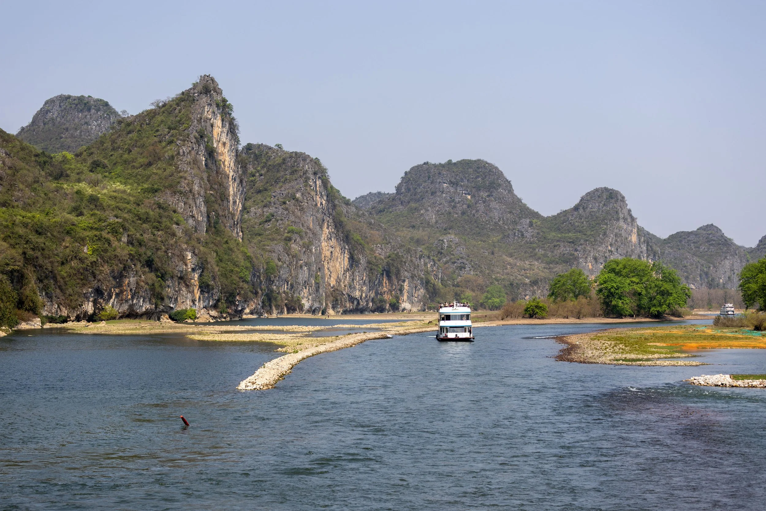 Boat on river surrounded by karst mountains and green trees in picturesque landscape.