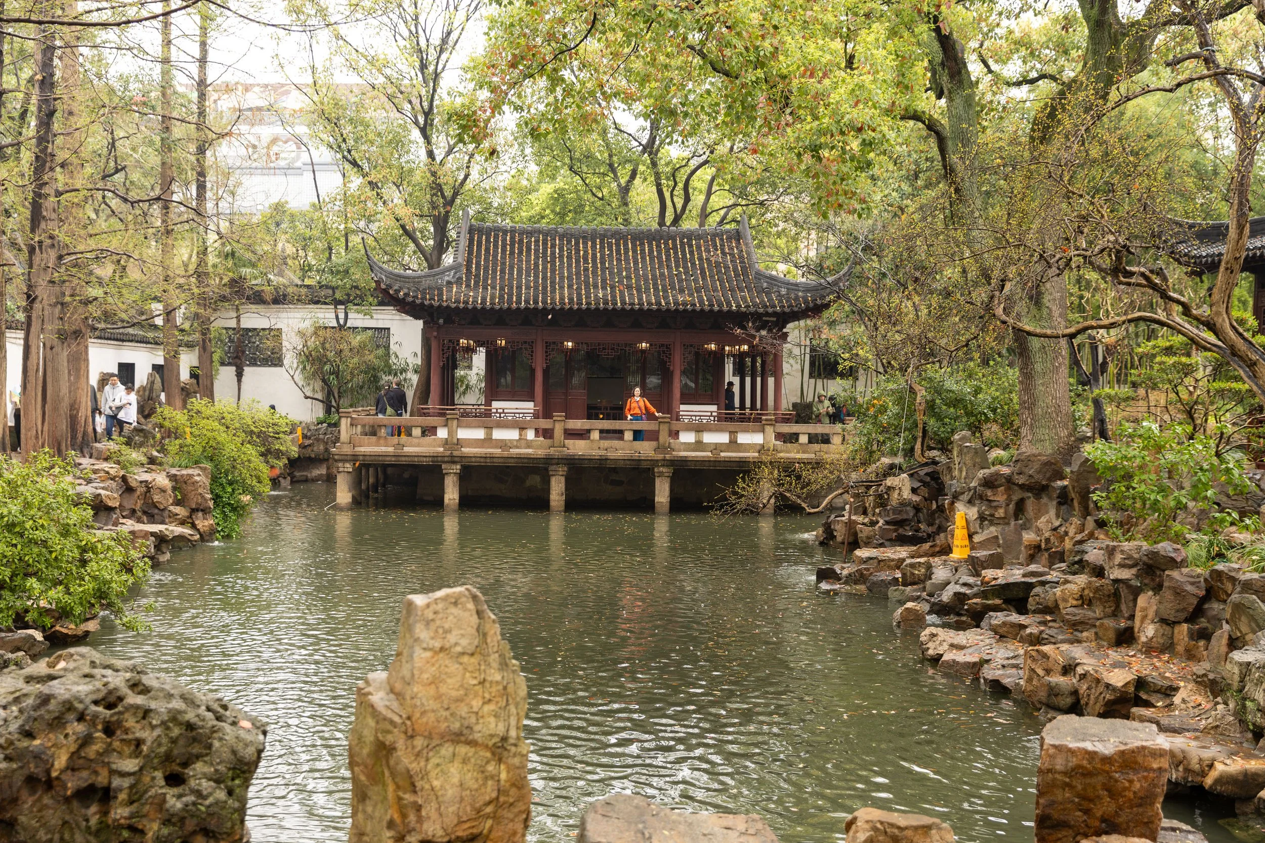 Traditional Chinese garden with pavilion over a pond, surrounded by rocks and trees.