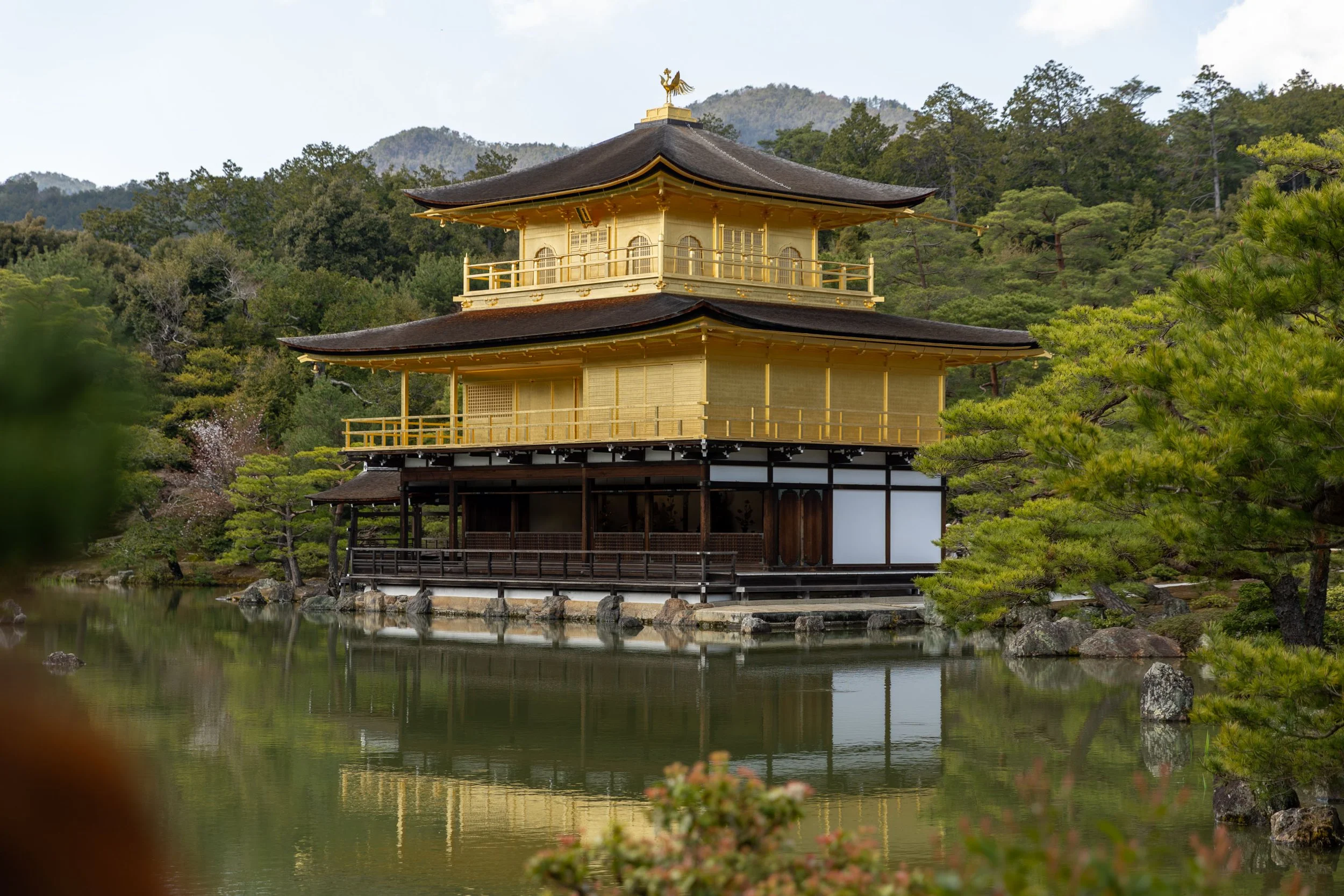 Kinkaku-ji, the Golden Pavilion, a famous Zen Buddhist temple in Kyoto, Japan, surrounded by a tranquil pond and lush greenery.
