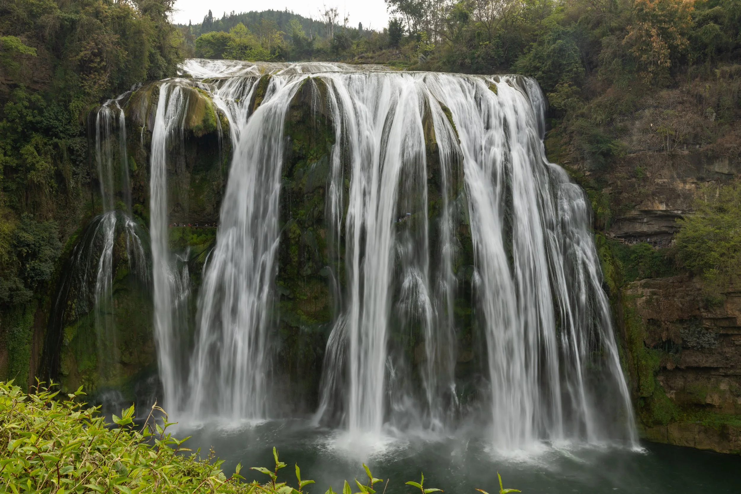 Large waterfall cascading over a rocky cliff surrounded by lush green vegetation.