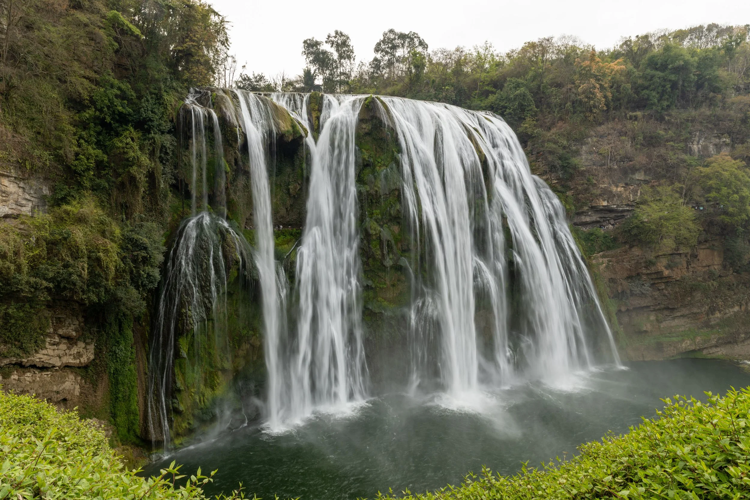 Scenic waterfall cascading over a moss-covered cliff surrounded by lush greenery.