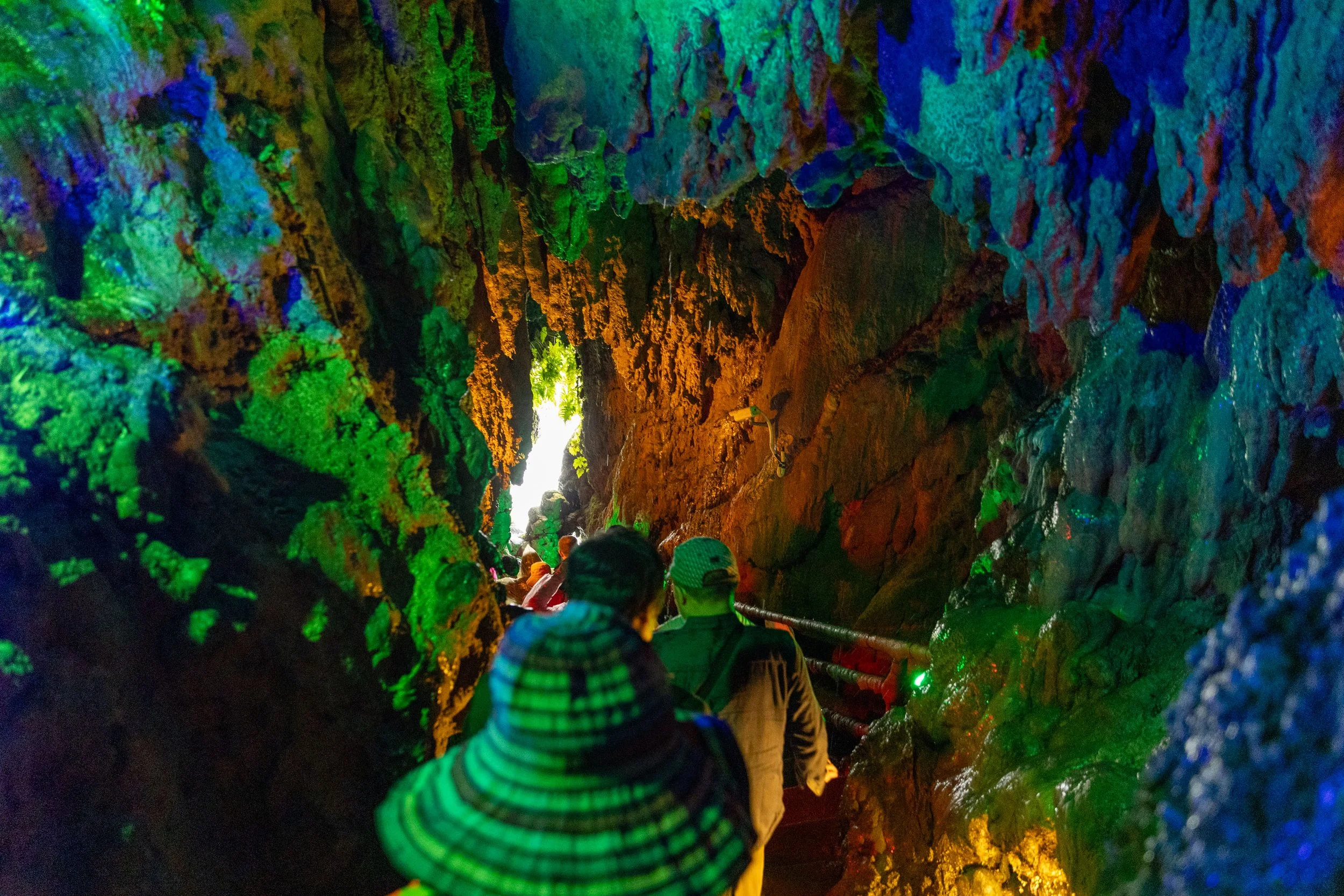 People exploring a colorful cave with green, blue, and orange rock formations.