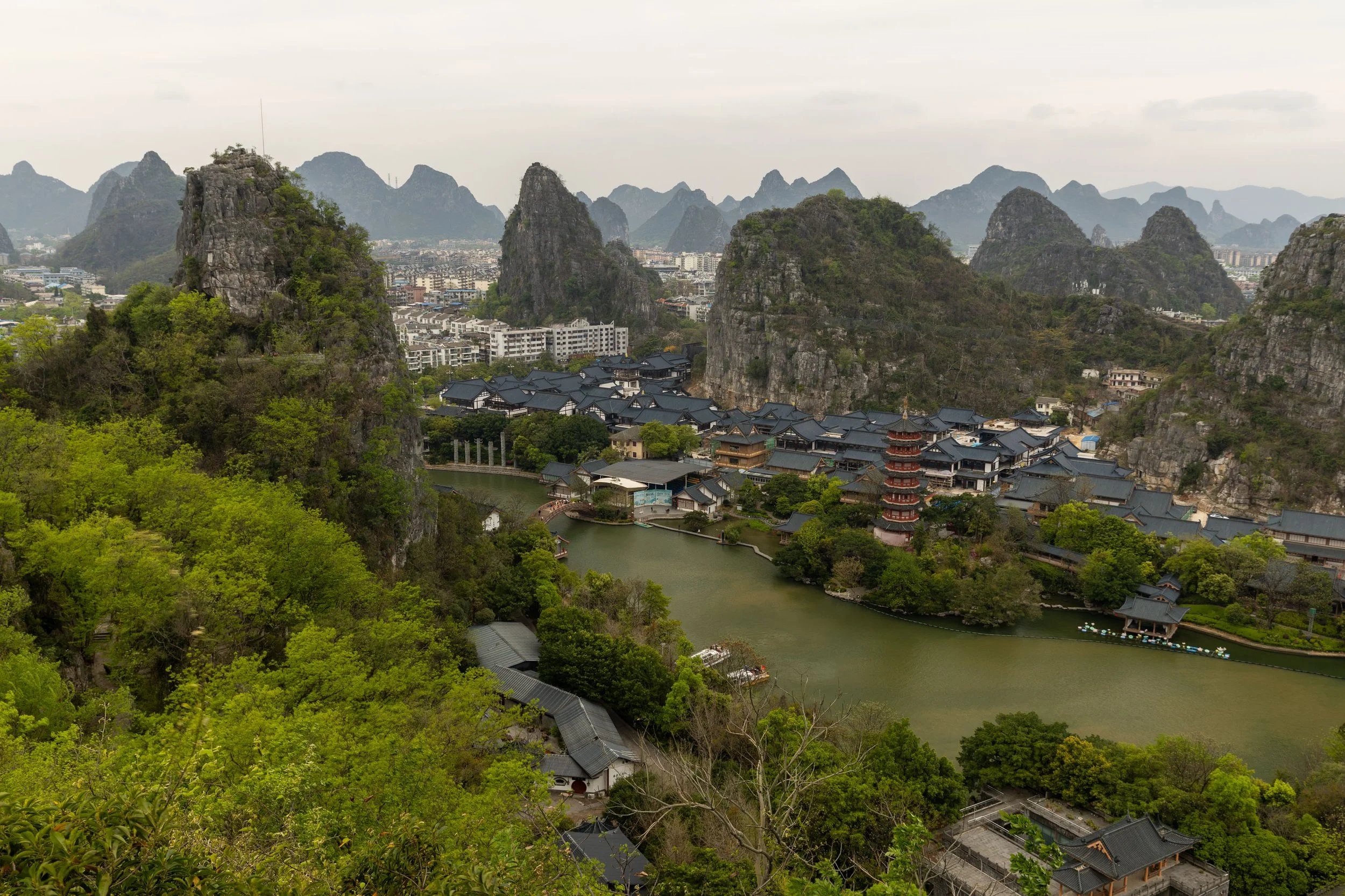 Aerial view of a traditional Chinese village with a pagoda, surrounded by lush green trees and karst mountains.