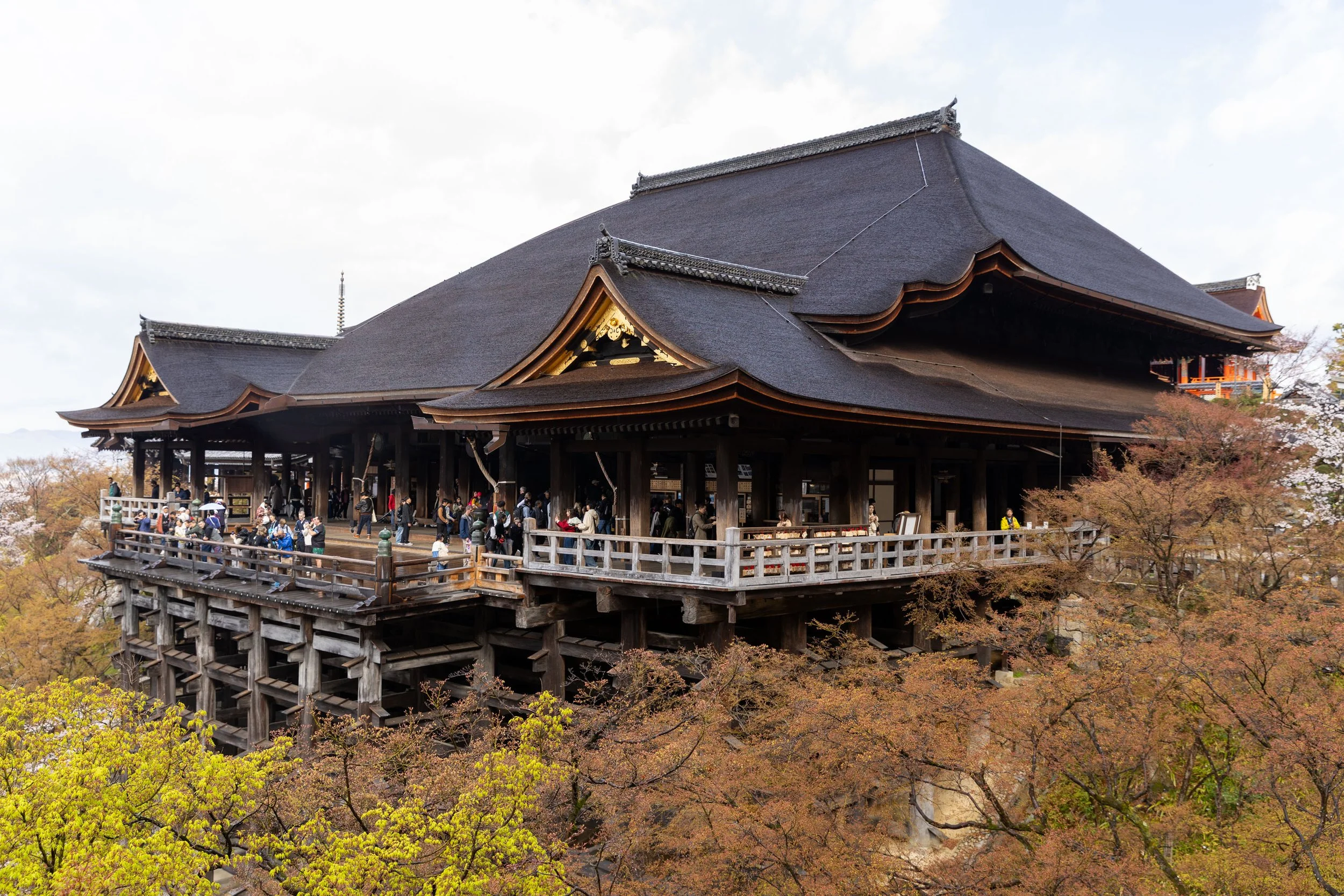 Kiyomizu-dera Temple in Kyoto, Japan, with tourists and surrounding trees in spring.