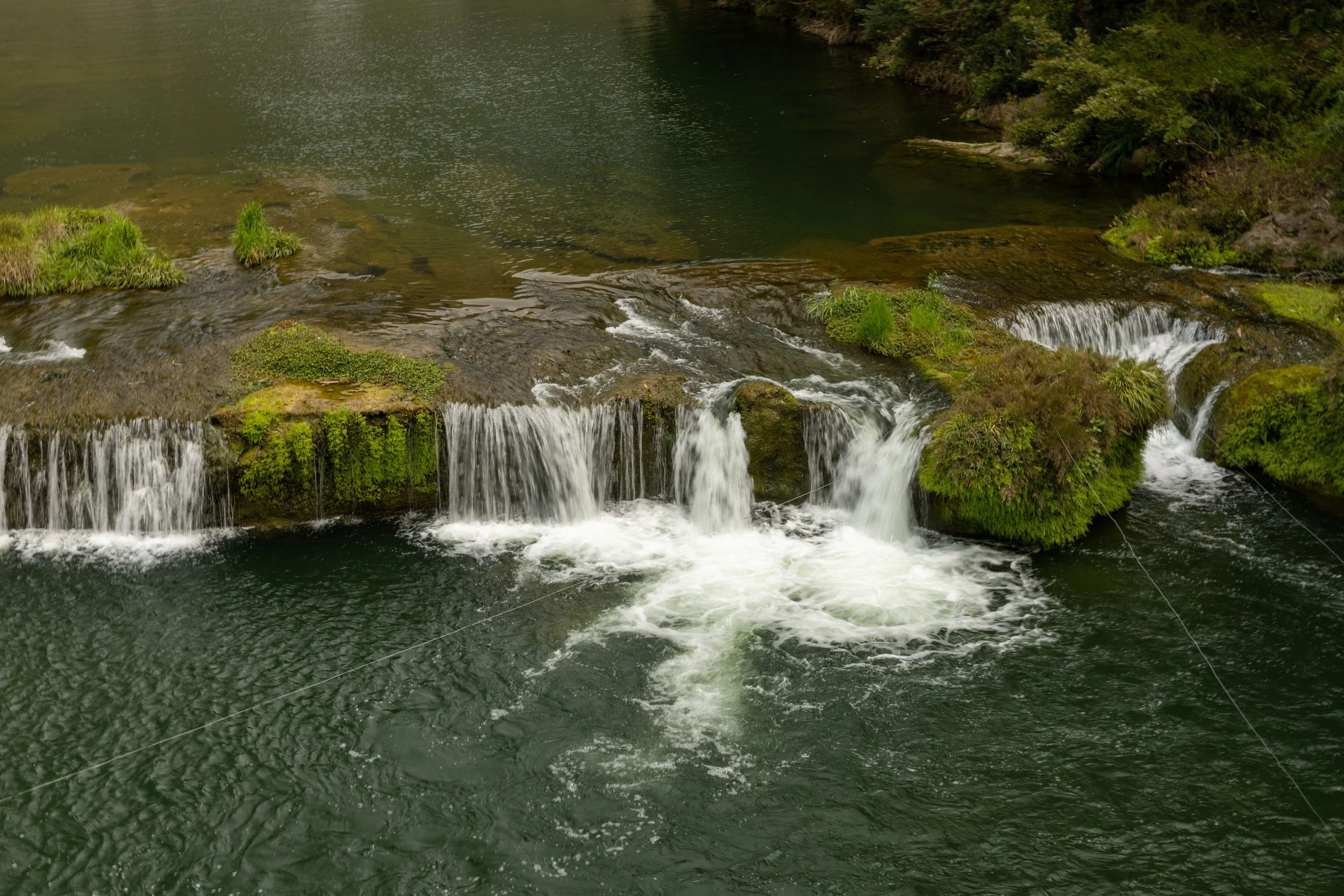Small waterfall with lush green moss-covered rocks in a river.