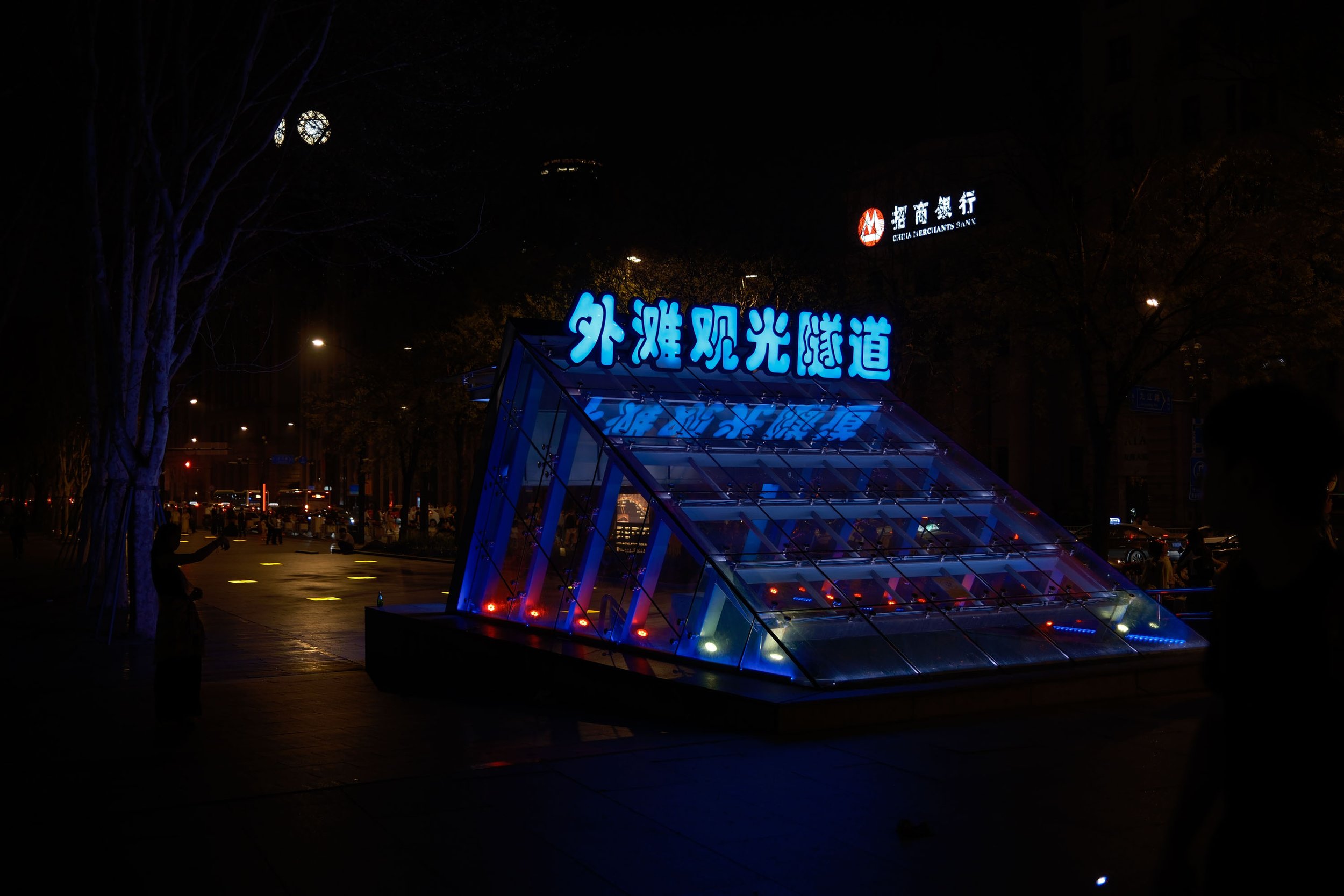Illuminated entrance with Chinese characters and glass pyramid structure at night in an urban area.