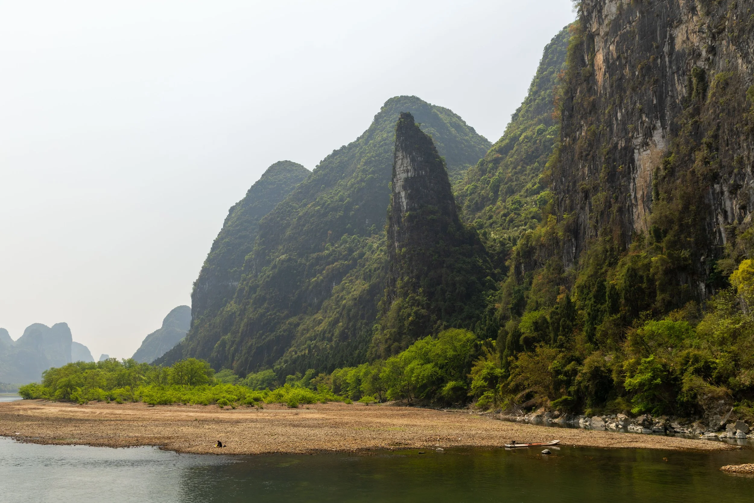 Landscape of karst mountains along a river, with lush green vegetation and rocky shores.