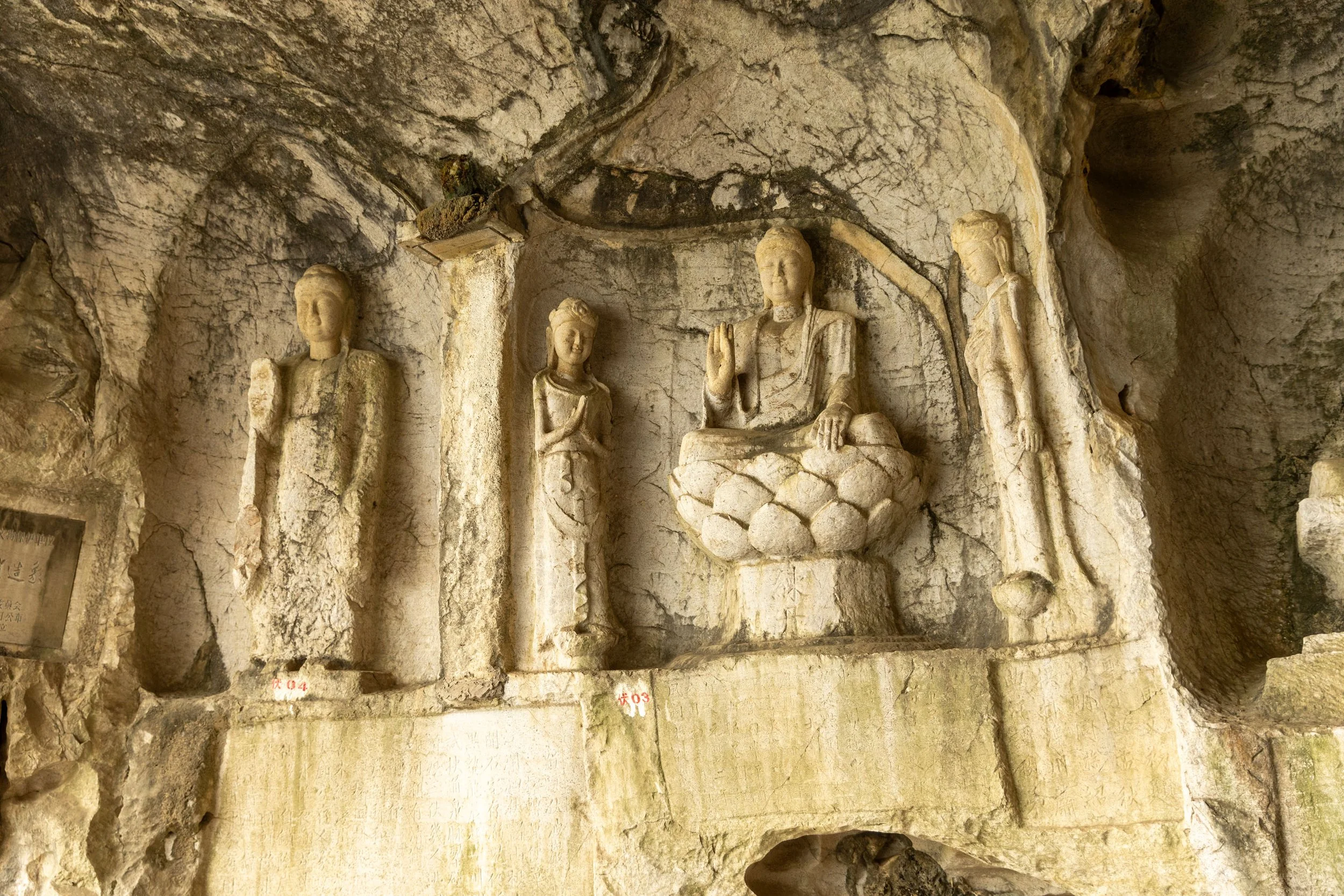 Ancient stone carvings of Buddhas and figures in a cave wall.