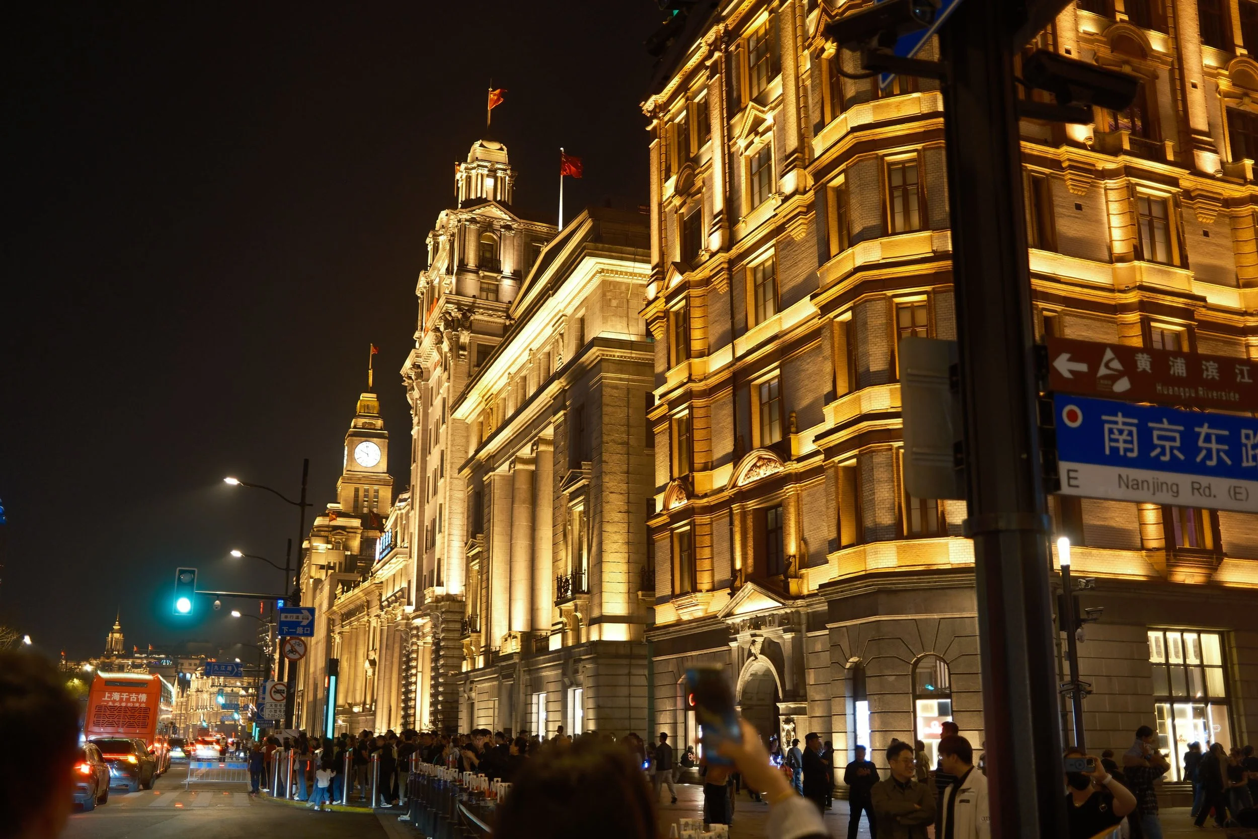 Night view of illuminated historic buildings on Nanjing Road East in Shanghai, with people and traffic on the street.