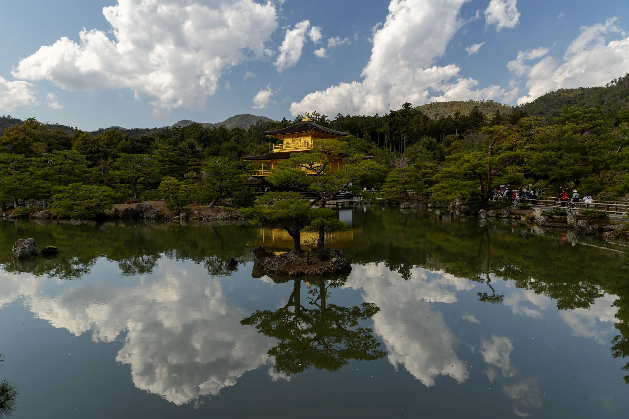 Kinkaku-ji Golden Pavilion reflecting on pond, surrounded by trees and clouds, Kyoto, Japan.