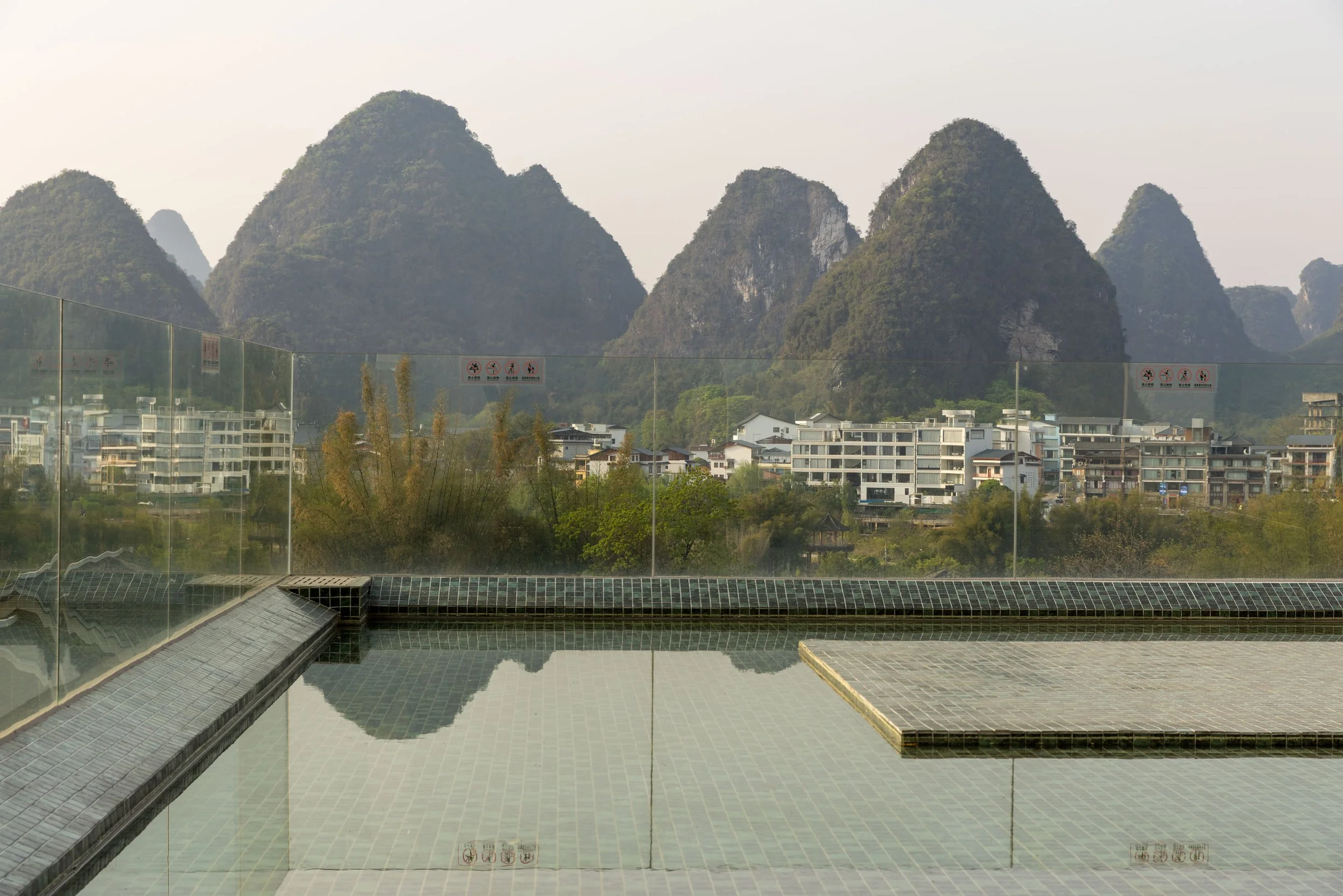 Scenic view of karst mountains and a town with glass railing and reflecting pool in the foreground.