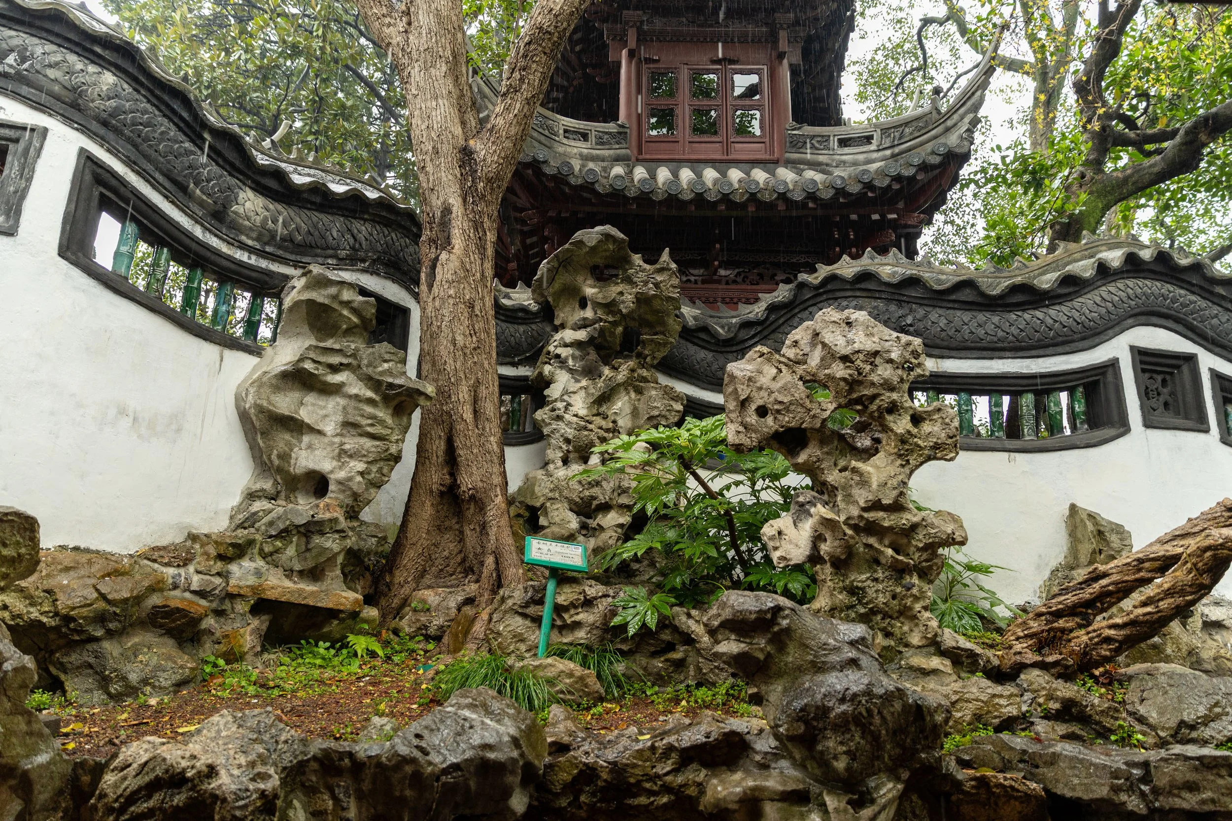Traditional Chinese garden with ornate roof, rock formations, and greenery.