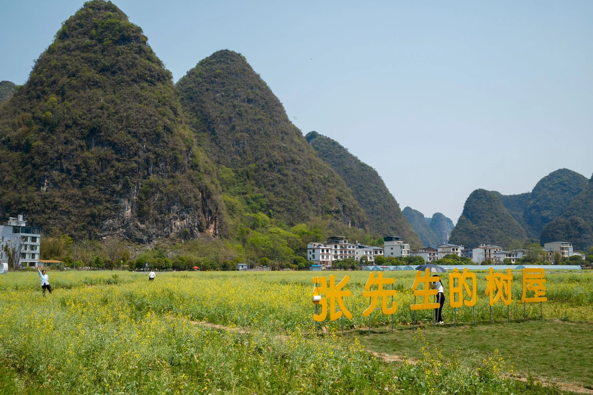Scenic view of karst mountains, green fields, and a village with Chinese characters on a sign in the foreground.