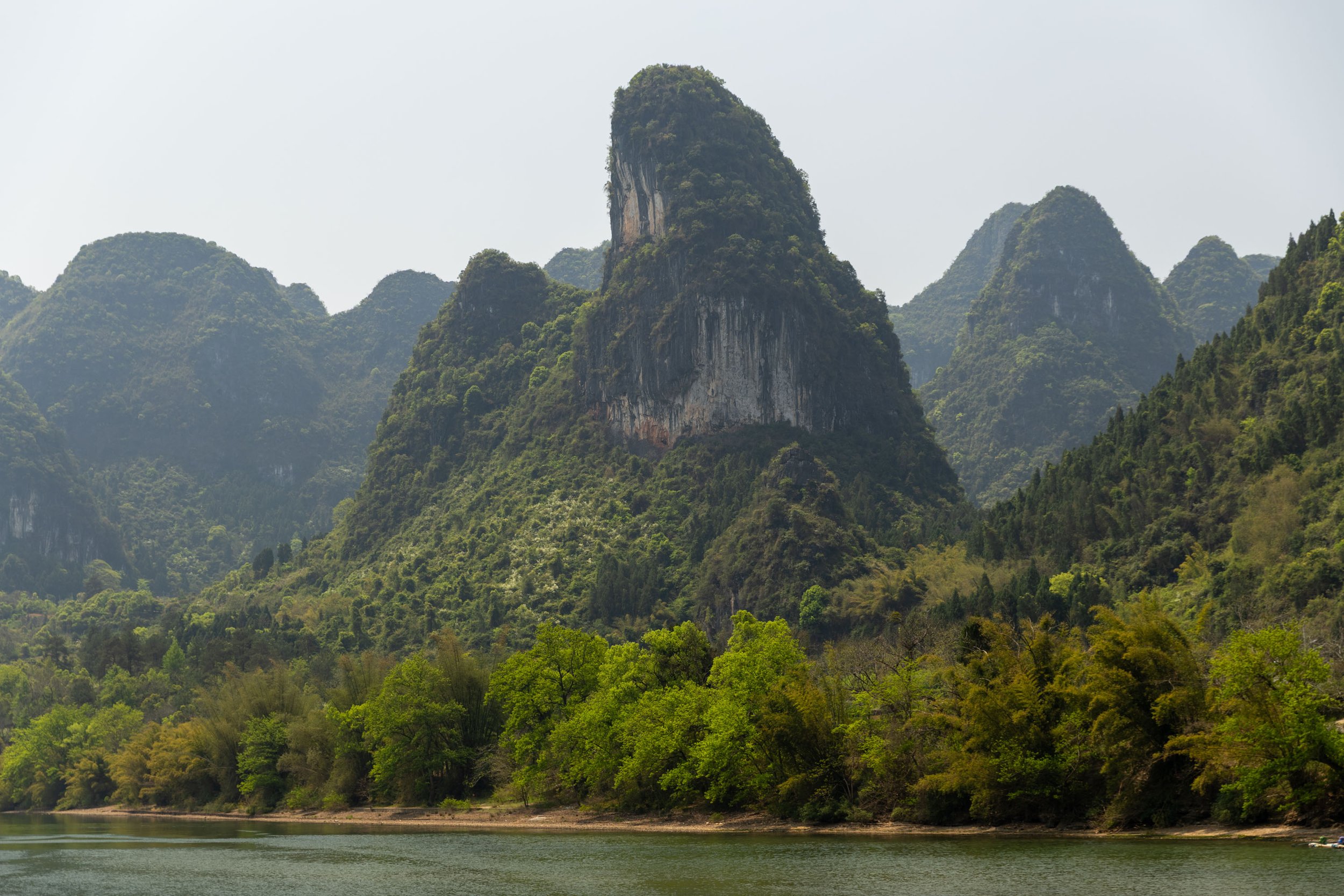 Lush green karst mountains by a river under a clear sky.