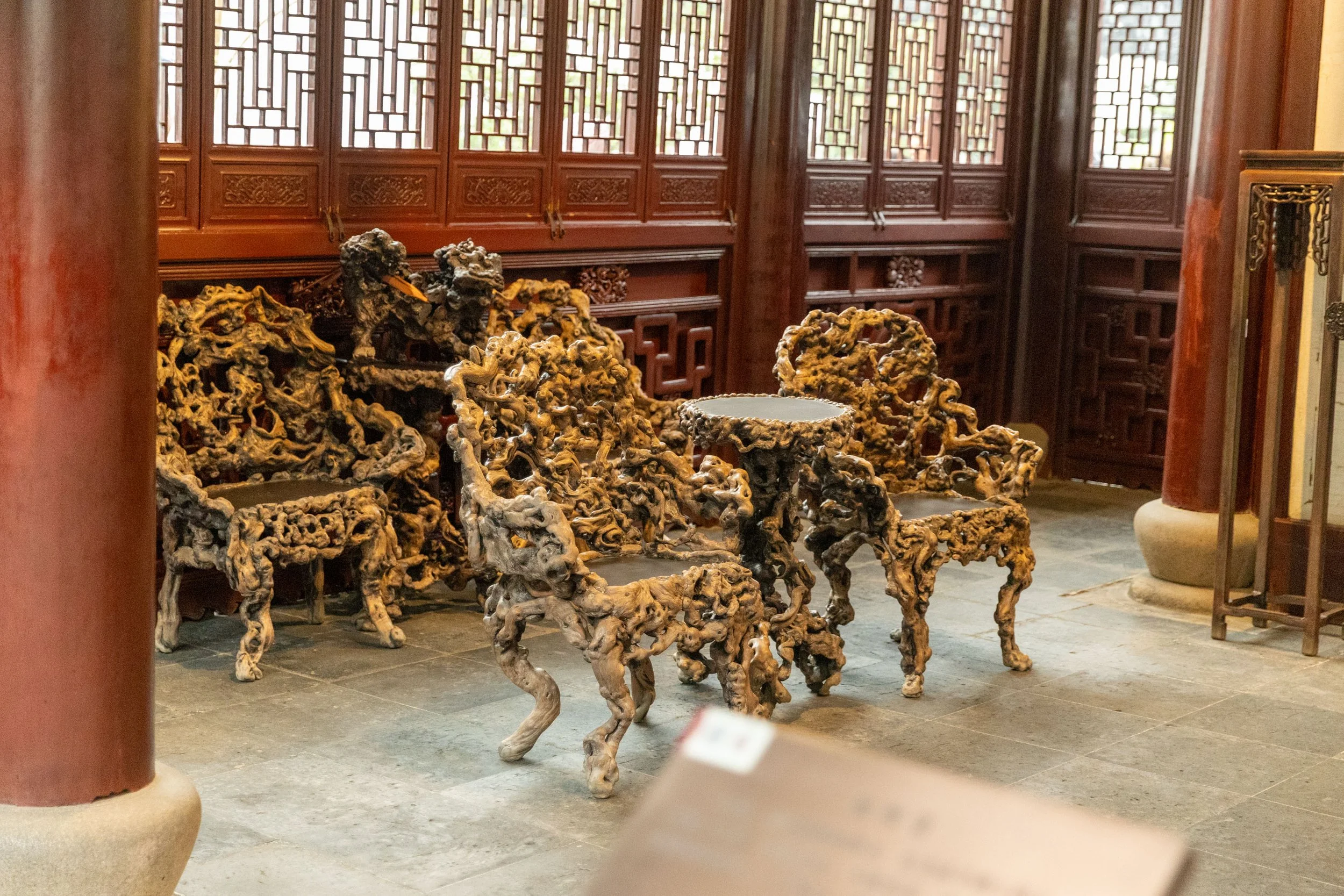 Intricately carved wooden chairs and table with ornate designs in a traditional Chinese room with wooden lattice window screens.
