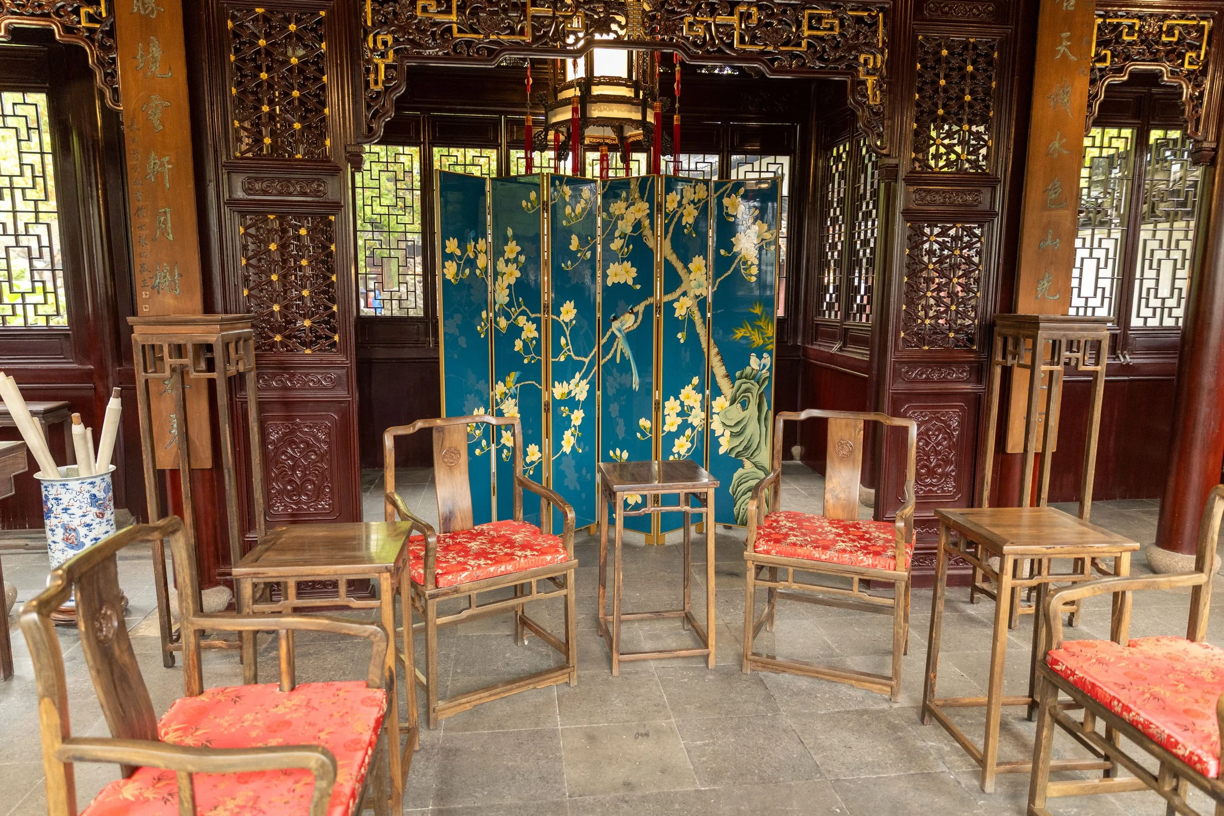 Traditional Asian interior with wooden chairs and tables, floral screen, and ornate latticework.