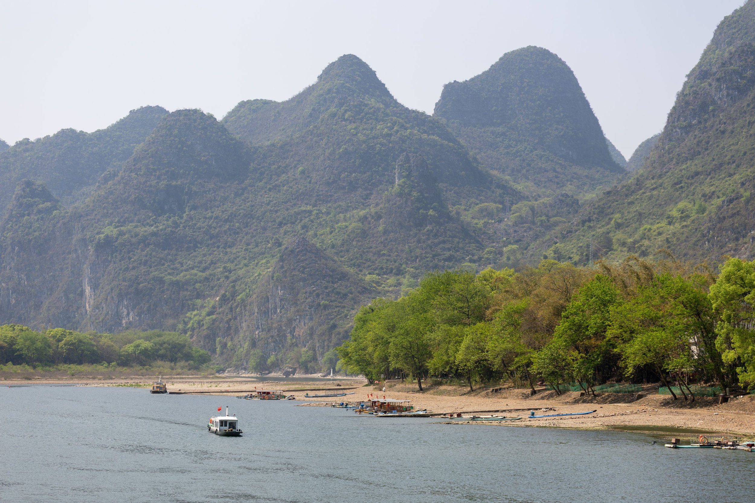A scenic view of a river with boats, surrounded by green forest and karst mountains.