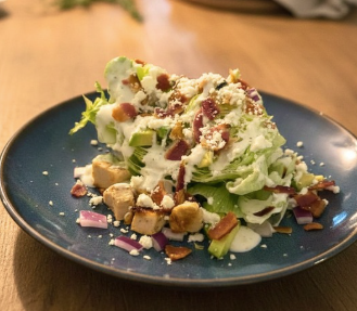 a wedge salad with bacon chicken and ranch dressing on a blue plate