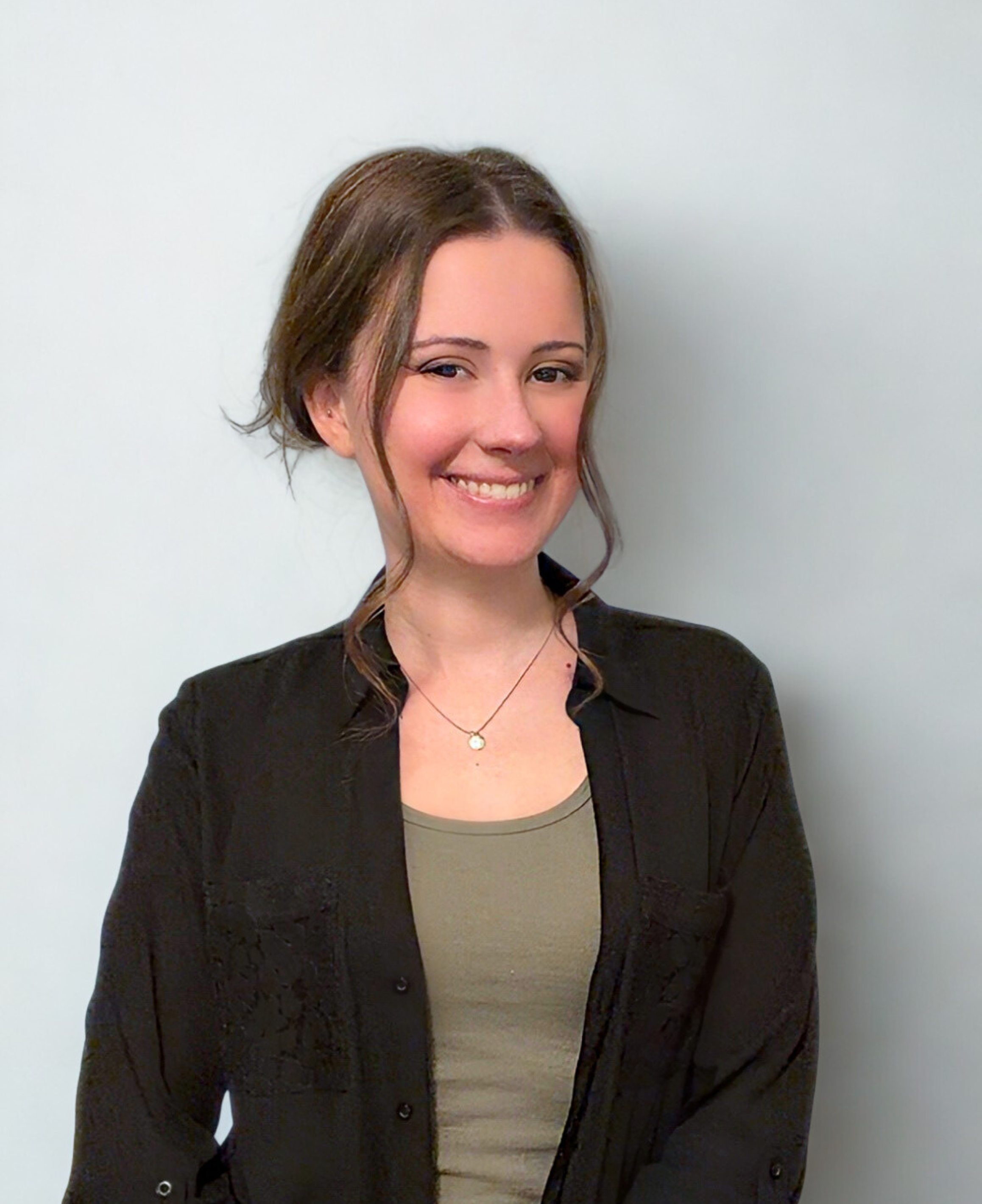 A professional style photo of a woman with brown hair and a black, collared button down shirt on, the background is light grey