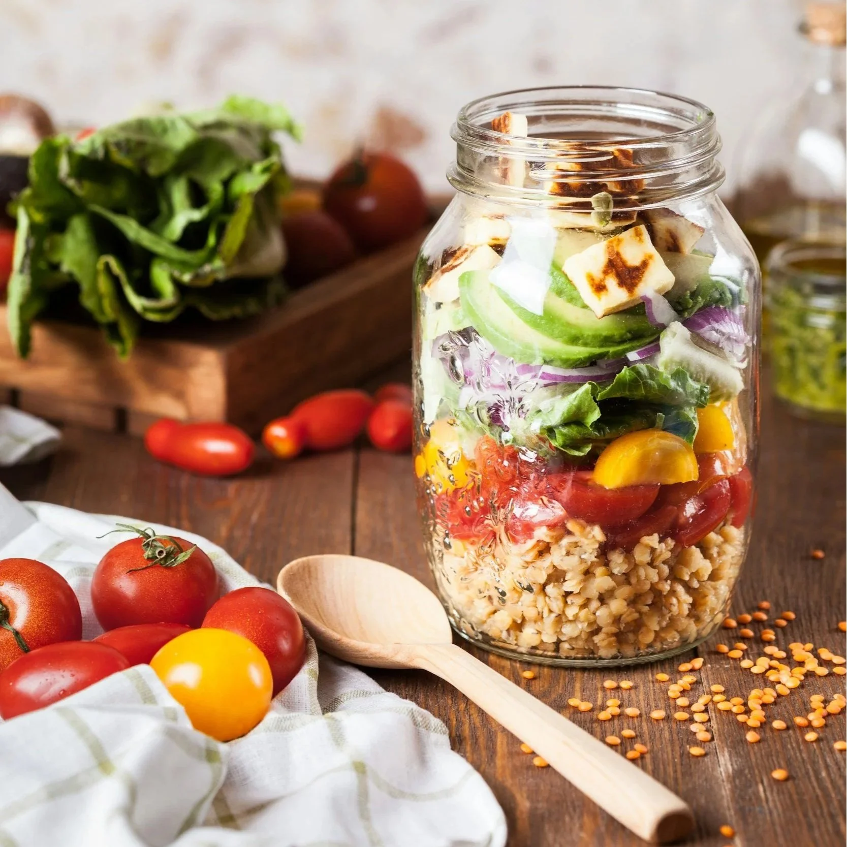 mason jar full of colorful mixed vegetables and quinoa with a wooden spoon and tomatoes on the table next to it