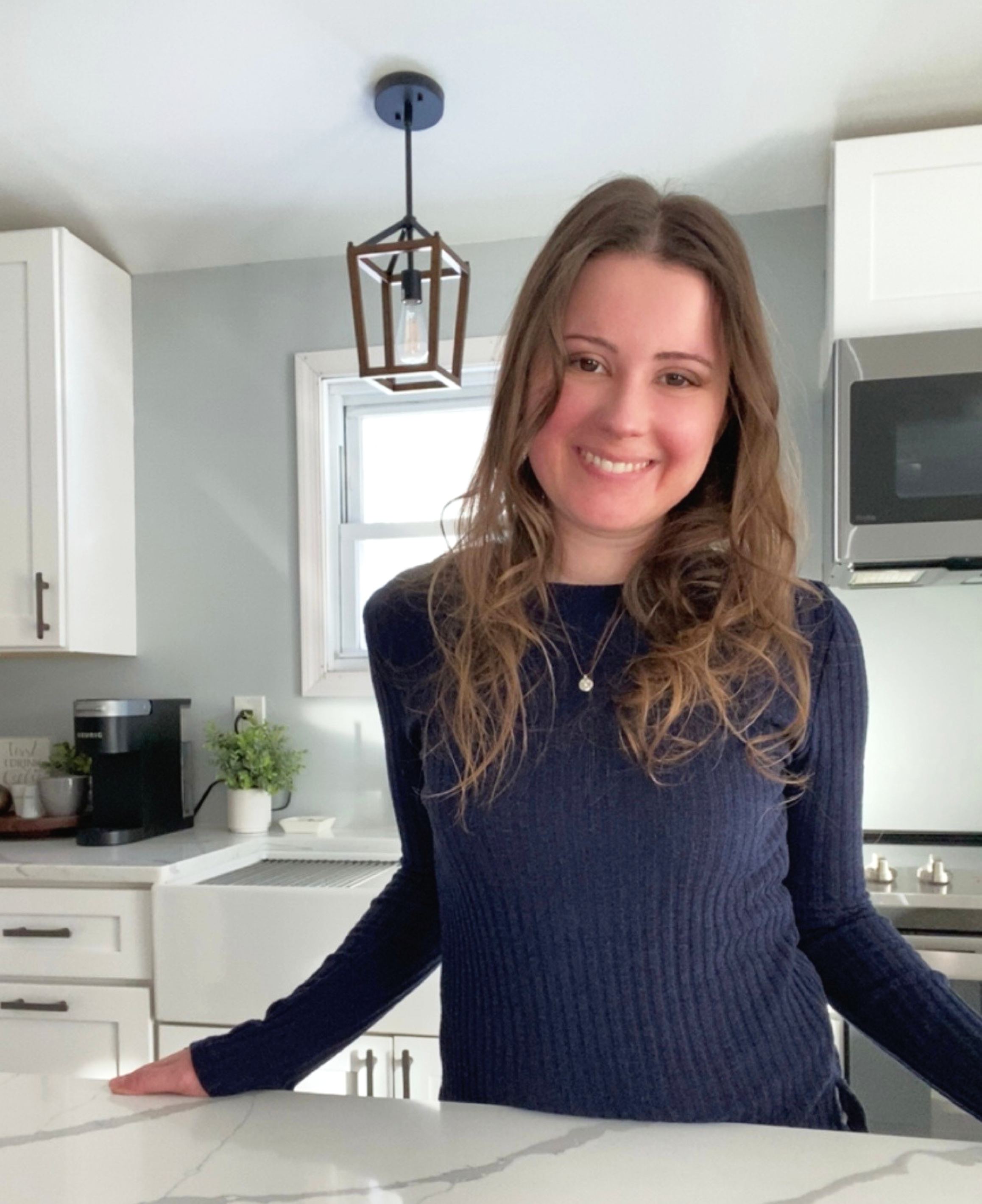 A friendly woman with brown hair in a navy sweater standing in the kitchen by the counter