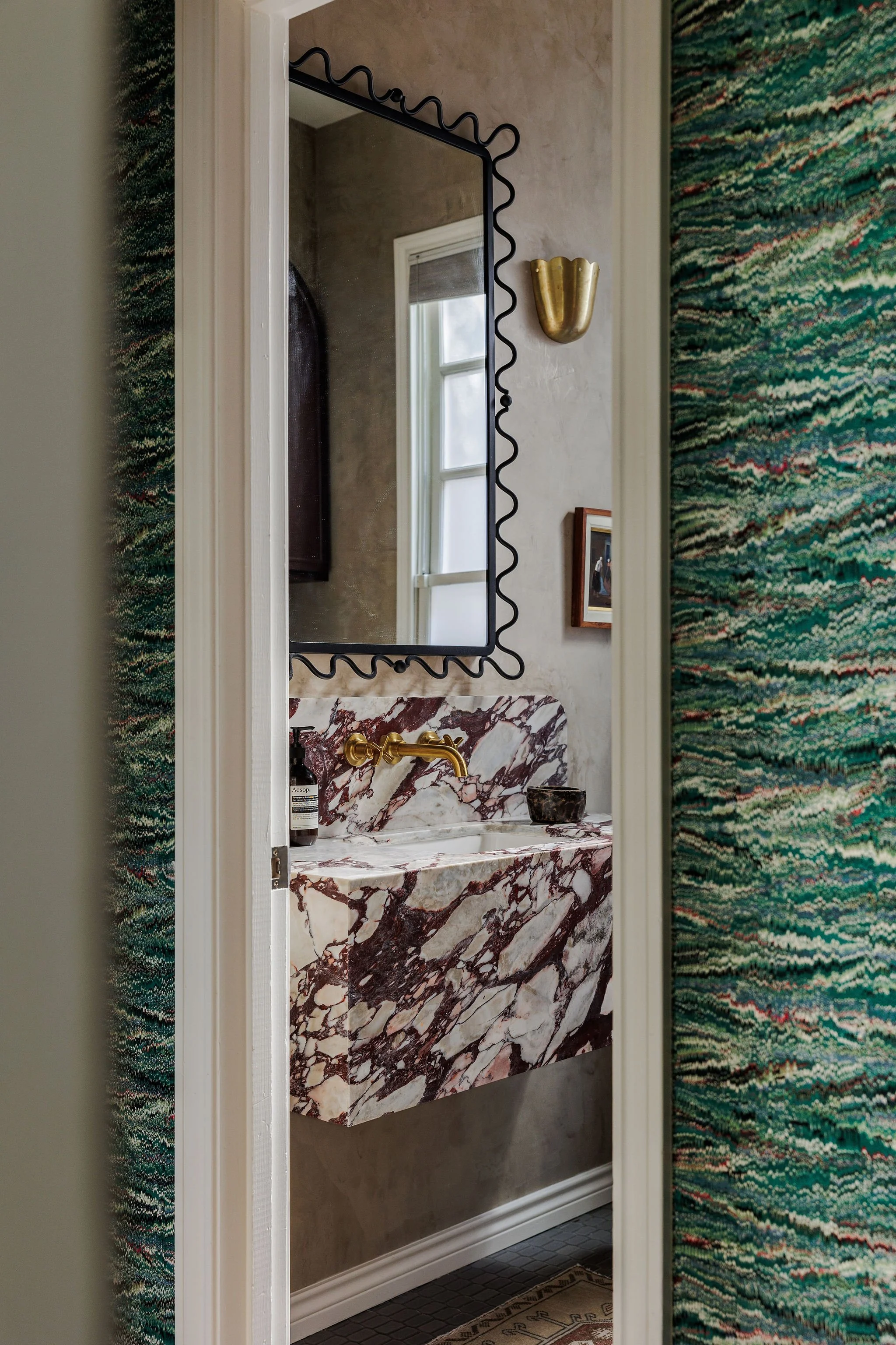 A bathroom vanity with a marble countertop and sink, a window, and a decorative wall mirror.