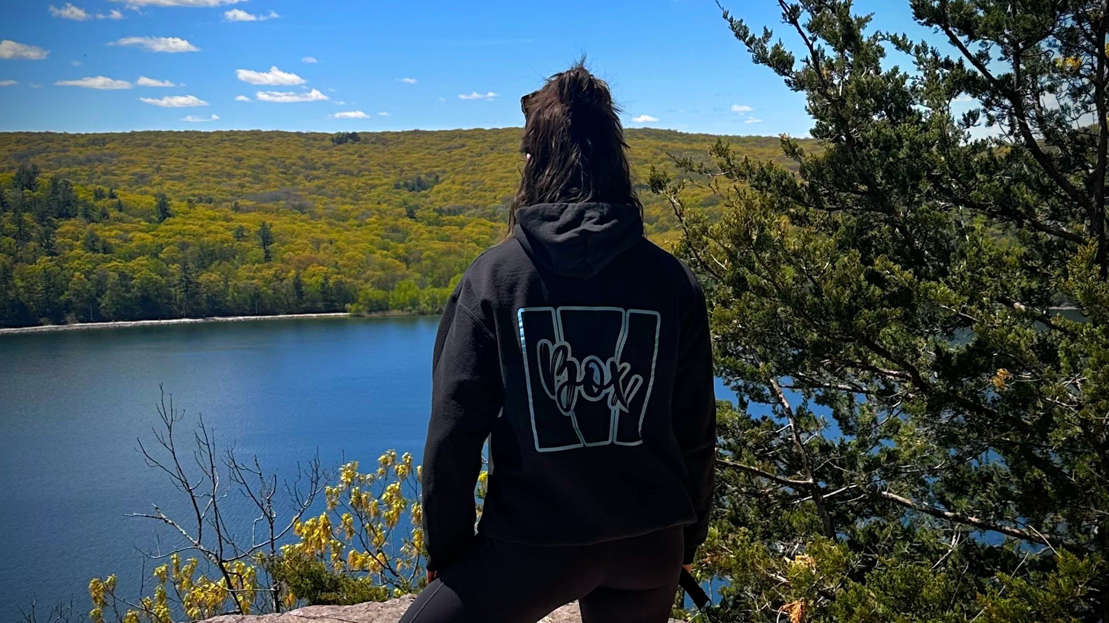 Owner of M Box Fitness wearing the M Box Logo Hoodie while overlooking a lake.